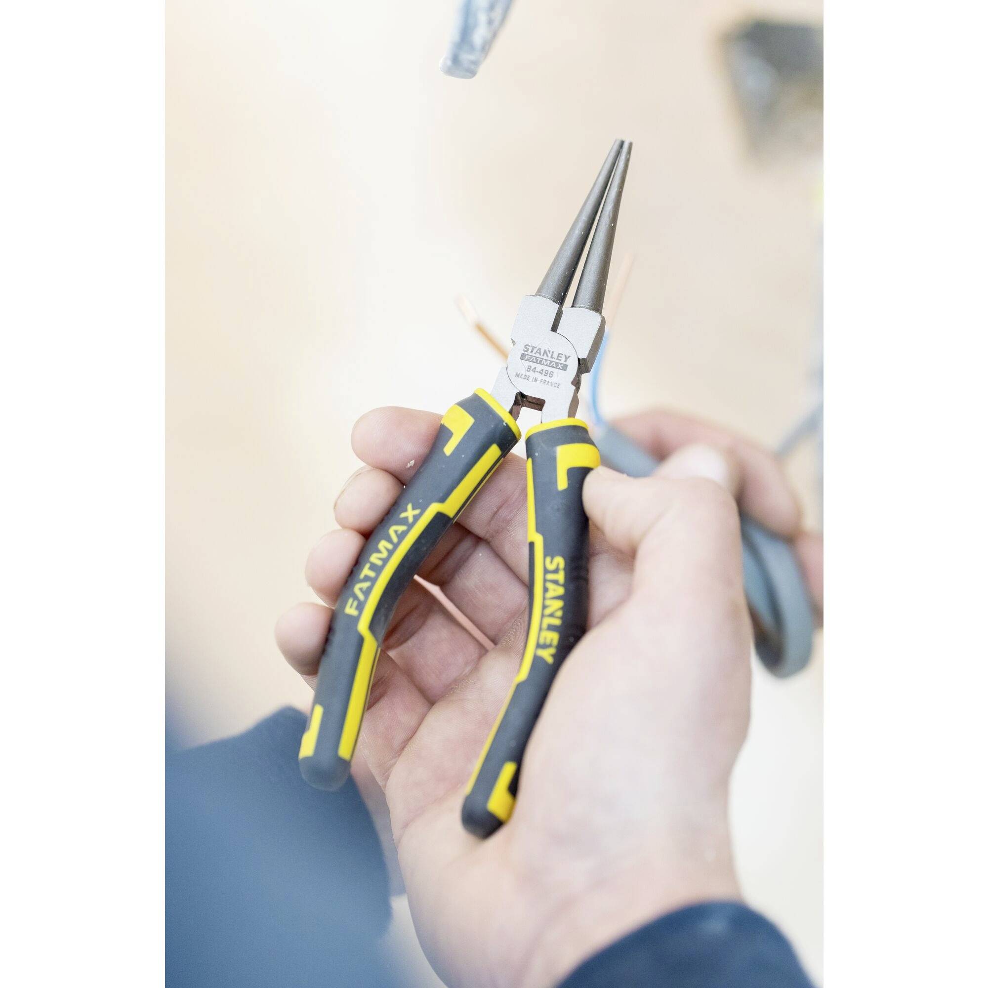 Eine Hand hält eine Zange mit langen, schmalen Backen, geeignet für Feinmechanikarbeiten. Das Werkzeug hat schwarze Griffe mit gelben Akzenten.