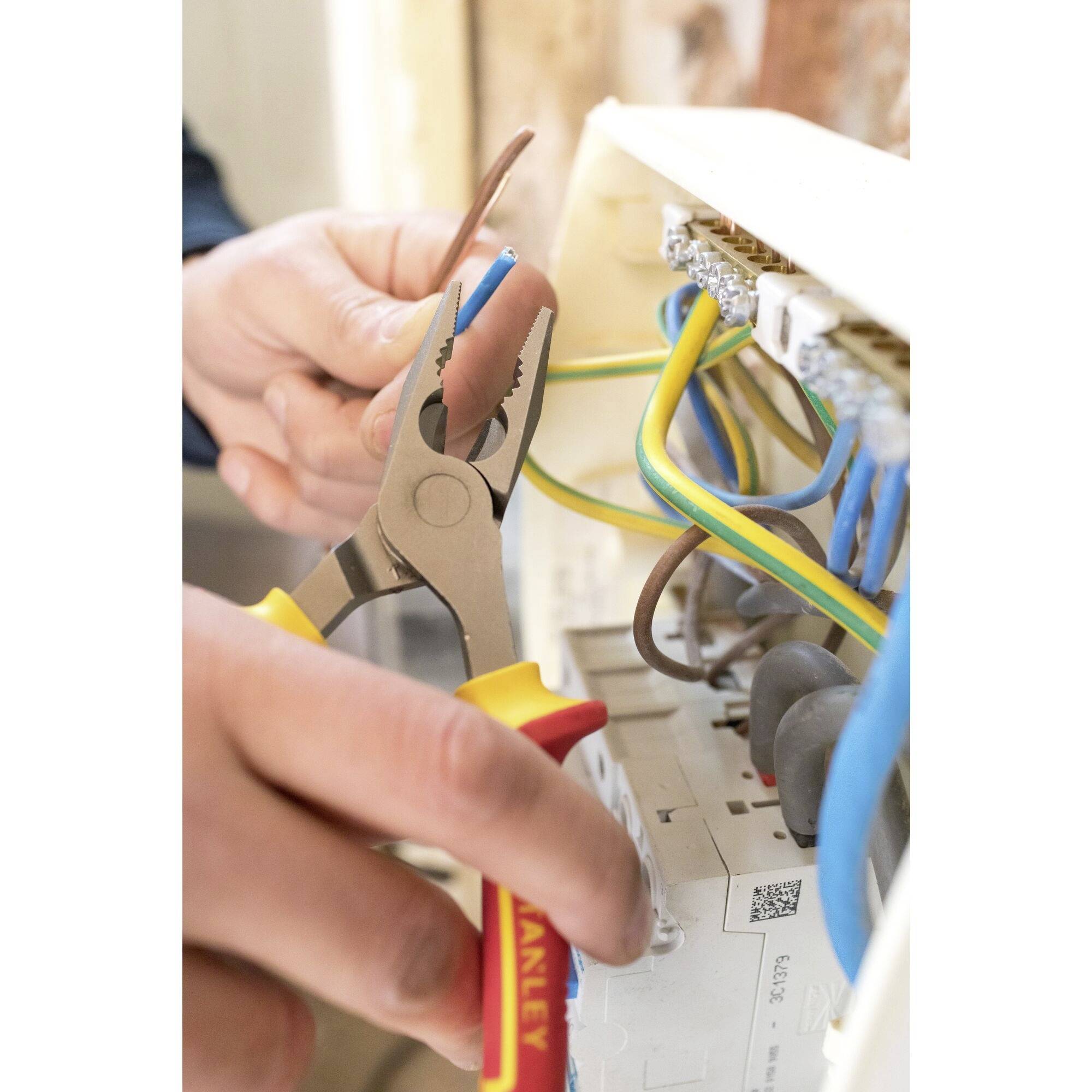 Person arbeitet mit einer Zange an elektrischen Kabeln in einem Sicherungskasten, hält einen Schraubendreher.