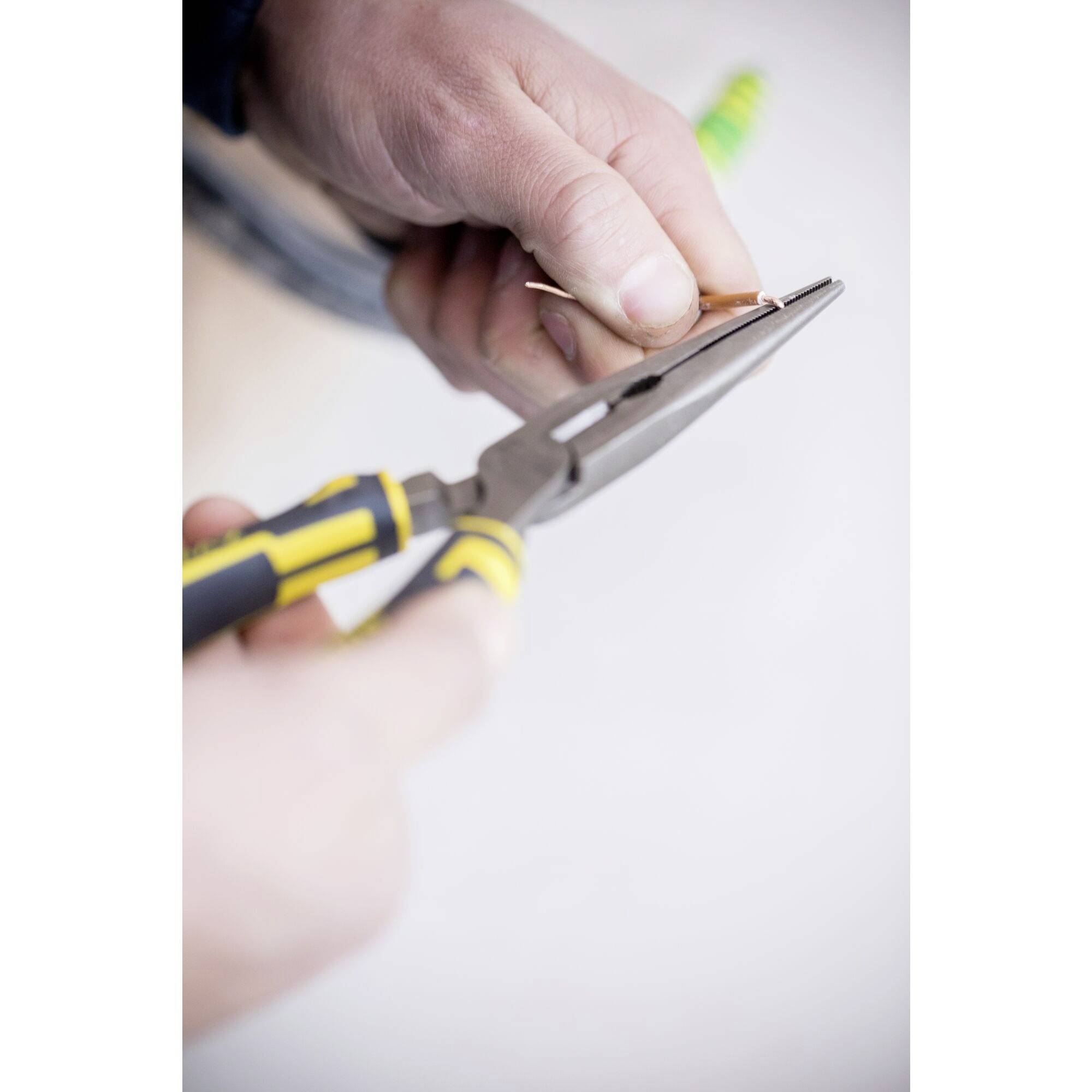 Eine Person hält eine Zange und biegt ein dünnes Drahtstück, möglicherweise bei einer handwerklichen Tätigkeit oder Reparaturarbeit.