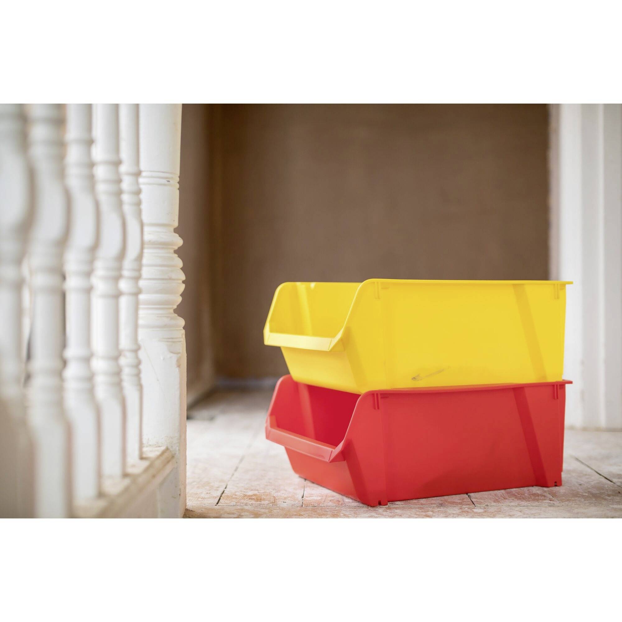 Zwei Plastikboxen, eine gelb und eine rot, gestapelt in einem leeren Flur. Links sind weiße Treppengeländer sichtbar.