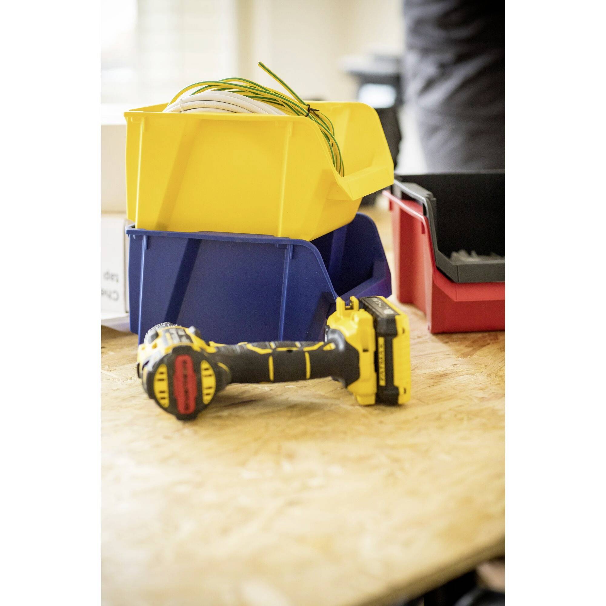 'Akkuschrauber und farbige Aufbewahrungsboxen auf einem Tisch; symbolisiert Handwerksarbeit oder Heimwerkerprojekt.'