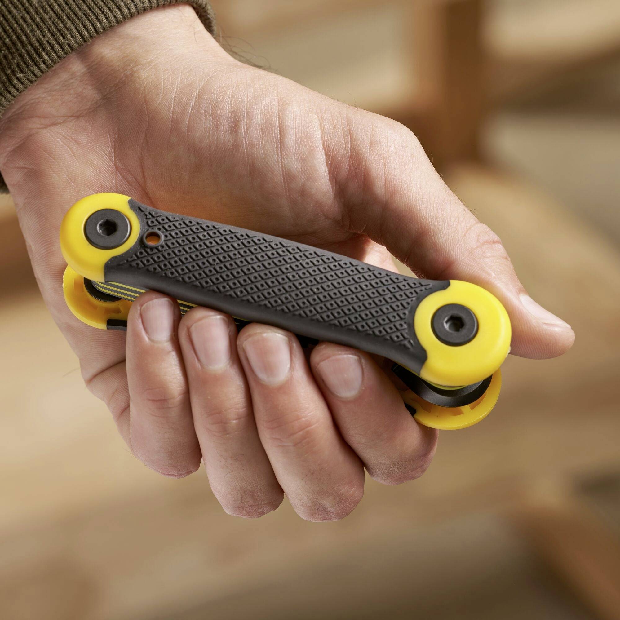 Eine Person hält ein gelbes Multifunktionstool mit mehreren Schraubendreherköpfen. Das Tool hat einen gummierten Griff für besseren Halt.
