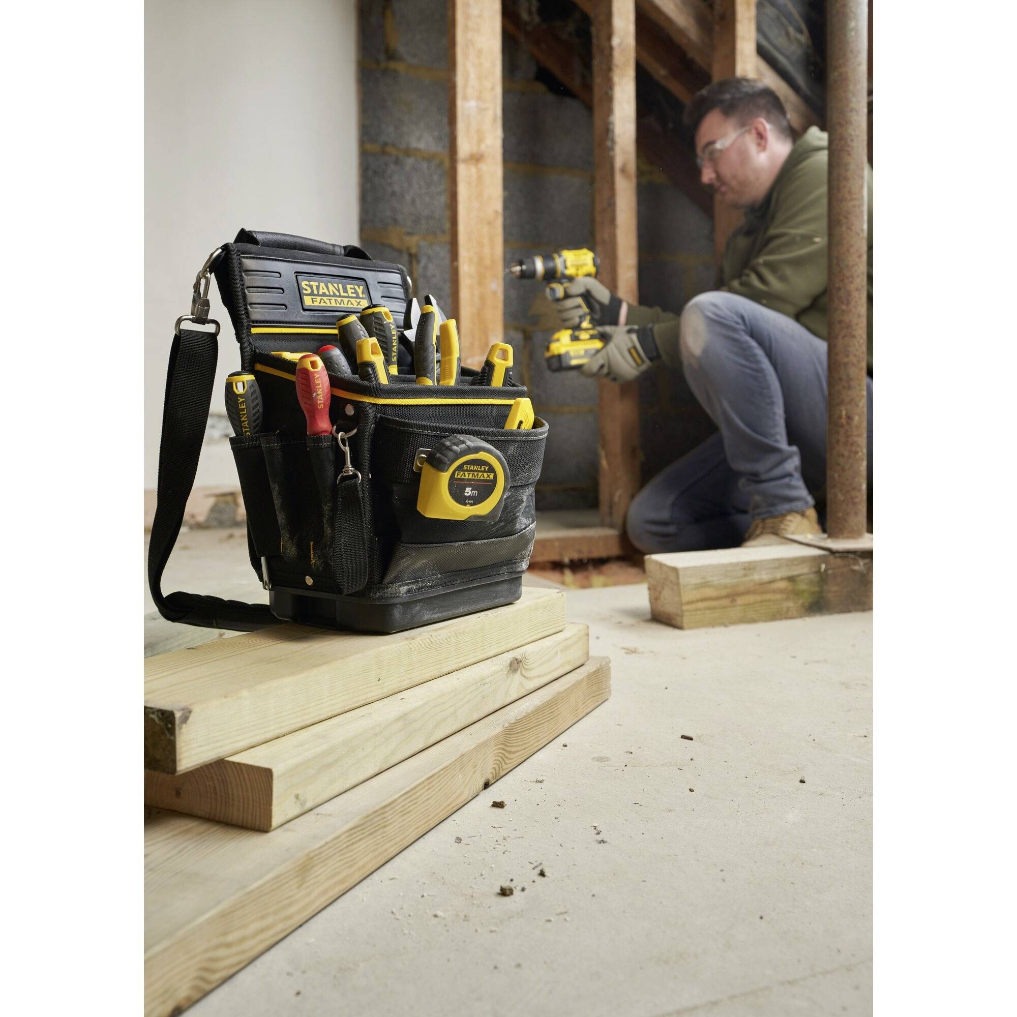 Ein Handwerker arbeitet mit einer Säge in einem Rohbau neben einem Werkzeugkoffer voller verschiedener Handwerkzeuge auf Holzbalken.
