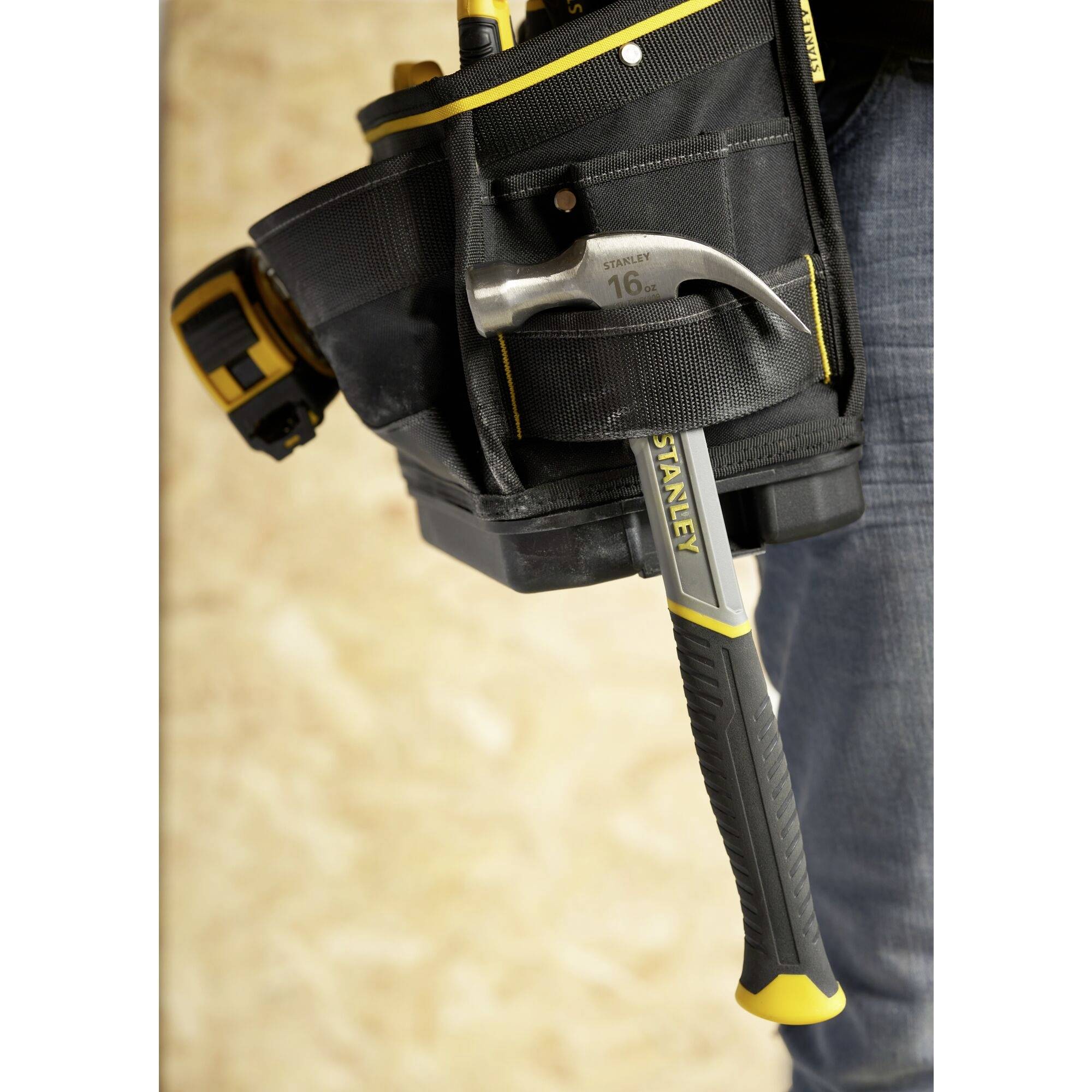 Ein Werkzeuggürtel mit einem Hammer aus Metall und Kunststoffgriff sowie mehreren Taschen, getragen von einer Person.