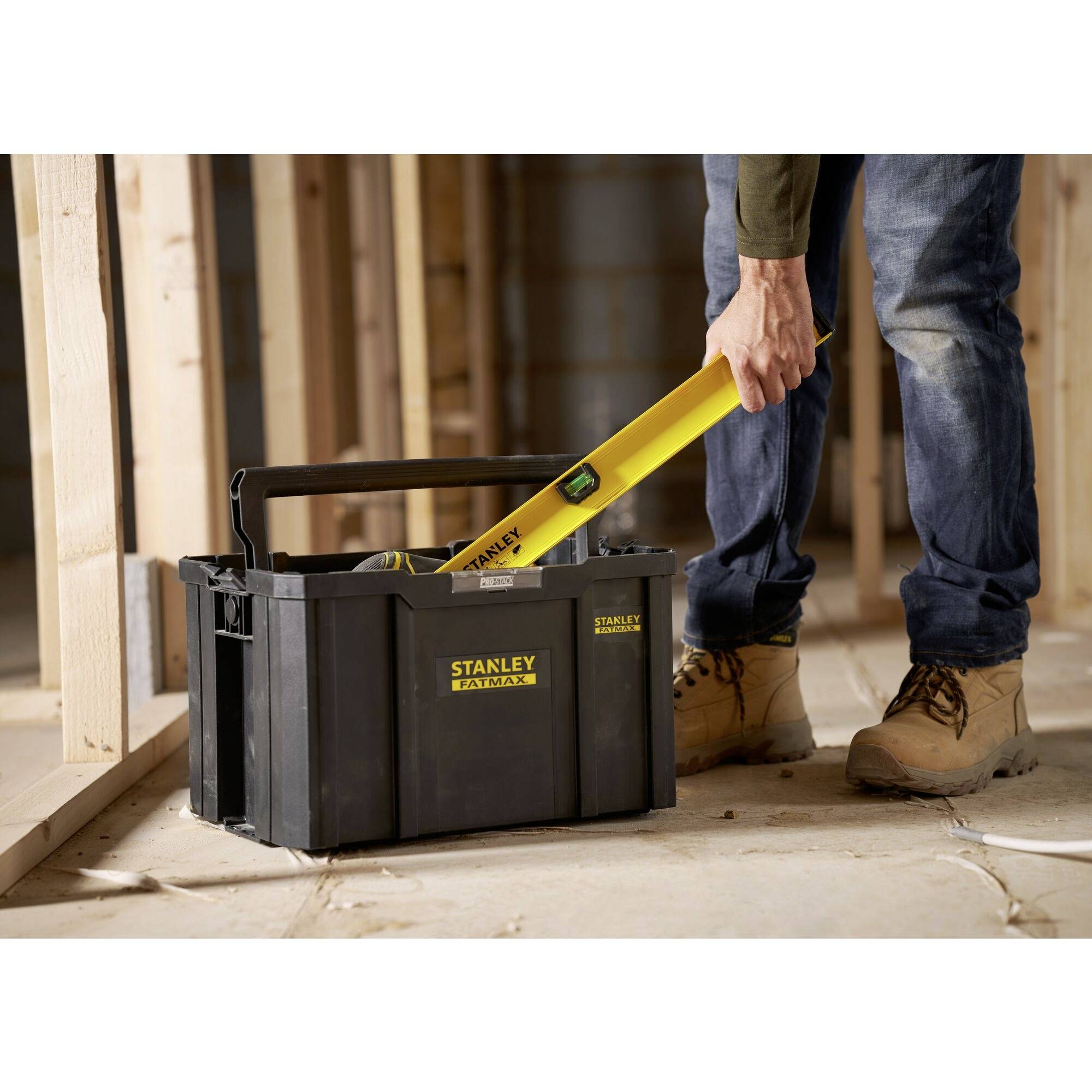 Ein Handwerker nimmt eine gelbe Wasserwaage aus einem schwarzen Werkzeugkasten in einem unfertigen Haus mit Holzständerwerk.