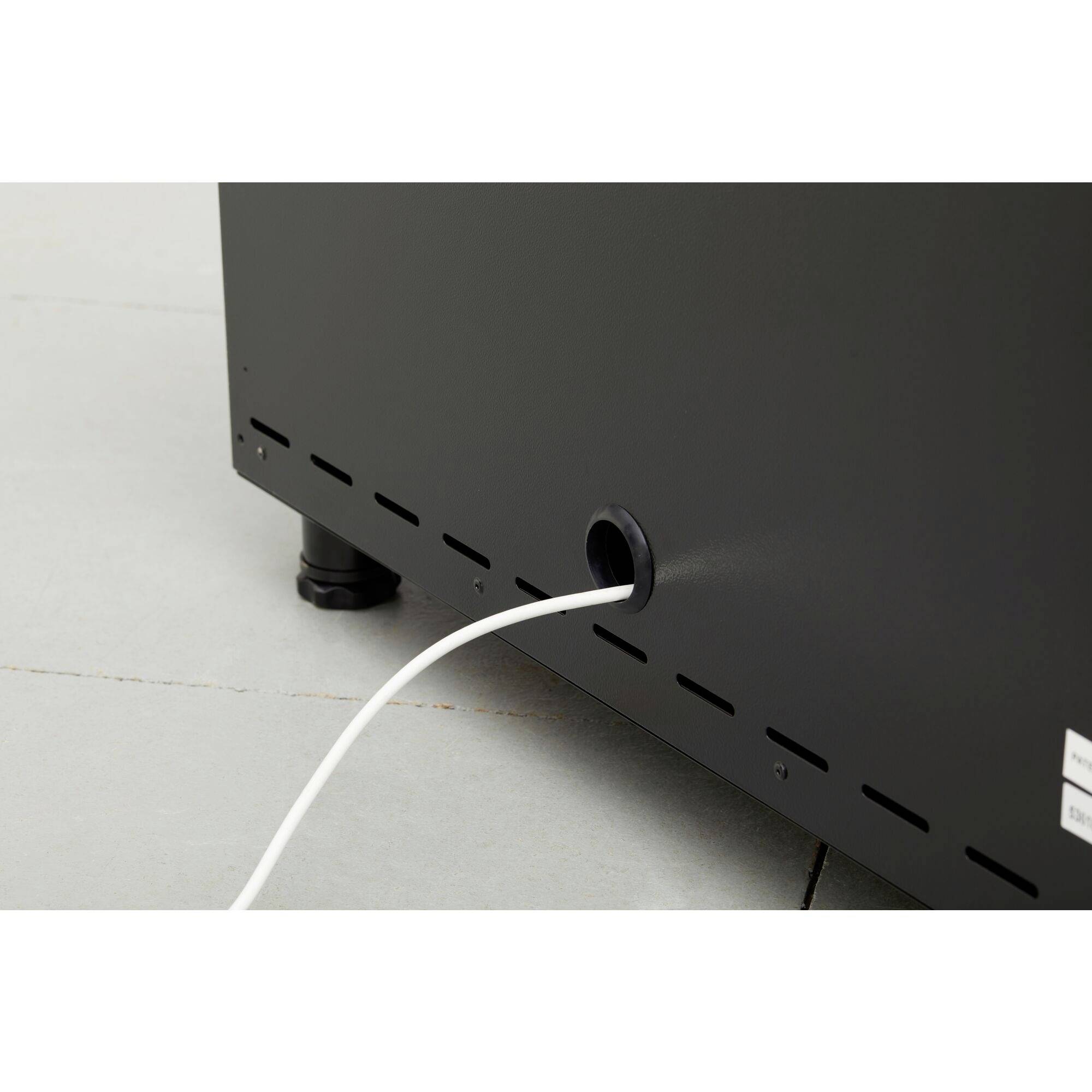 Ein weißes Kabel ragt aus einer Öffnung an der Seite eines schwarzen Geräts, das auf einem hellgrauen Boden steht.