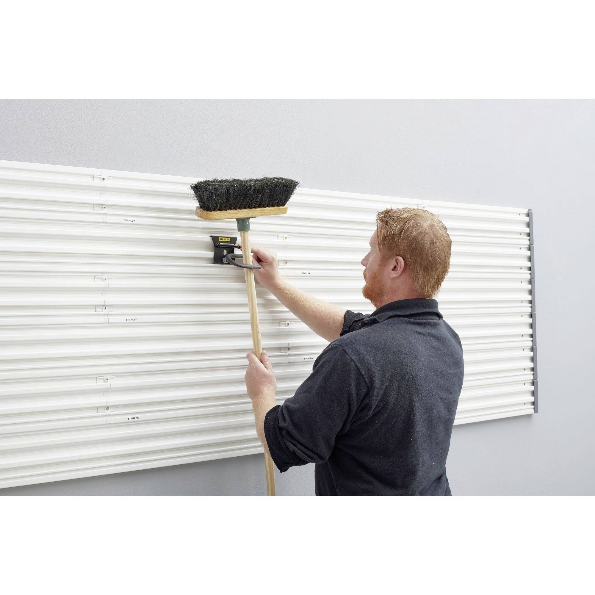 Eine Person in Arbeitskleidung verwendet einen Besen, um eine Heizkörperabdeckung an der Wand zu reinigen.