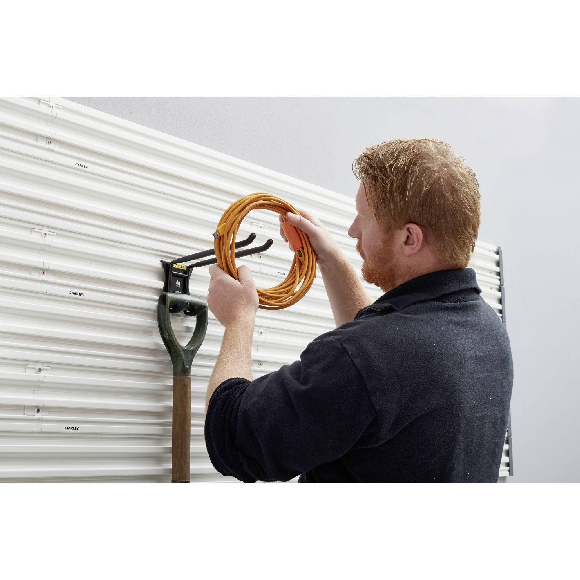 Ein Mann hängt ein orangefarbenes Kabel an einen Haken, der neben einem an der Wand befestigten Spaten montiert ist.
