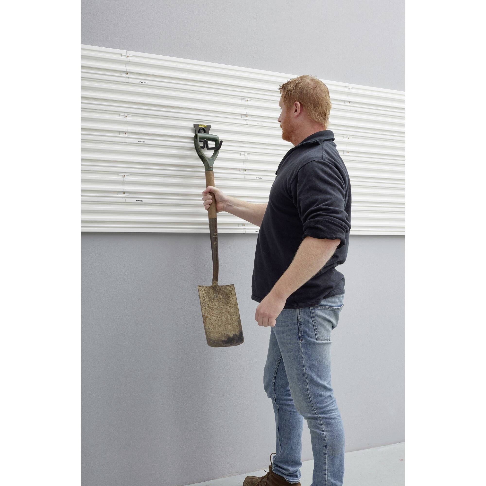 Ein Mann in Jeans und dunklem Pullover hängt eine Schaufel an ein an der Wand montiertes Panel.