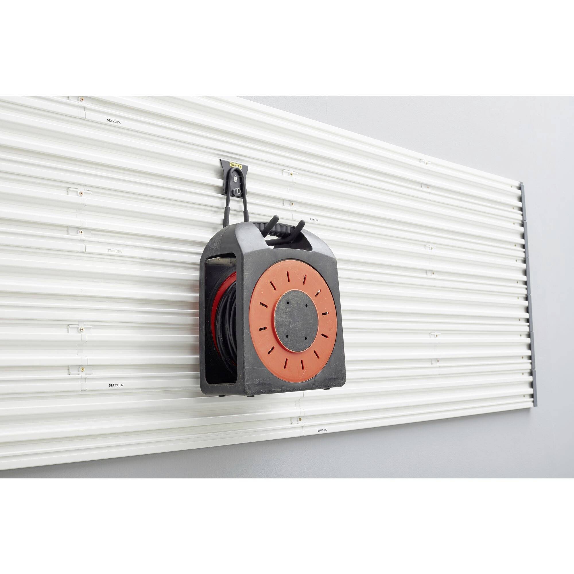 Ein schwarzes Kabeltrommelgehäuse mit orangefarbener Front hängt an einer strukturierten Metallwand.