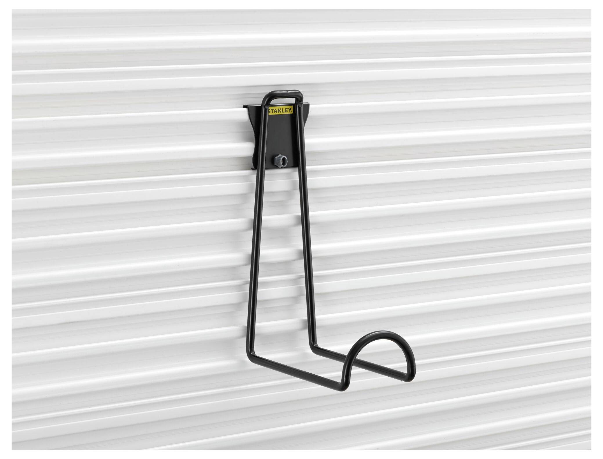 Eine schwarze Metallhalterung ist an einer geriffelten weißen Wand befestigt, geeignet zum Aufhängen von Gegenständen wie Schlauch oder Kabel.