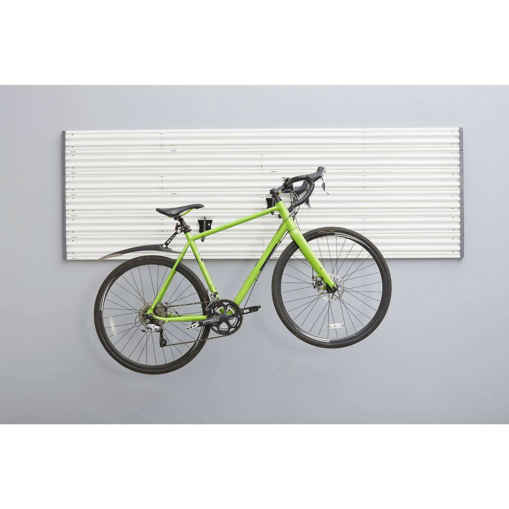 Grünes Rennrad hängt an einer grau-weißen Wandhalterung. Rahmen und Räder betonen das schlanke Design vor dem minimalistischen Hintergrund.