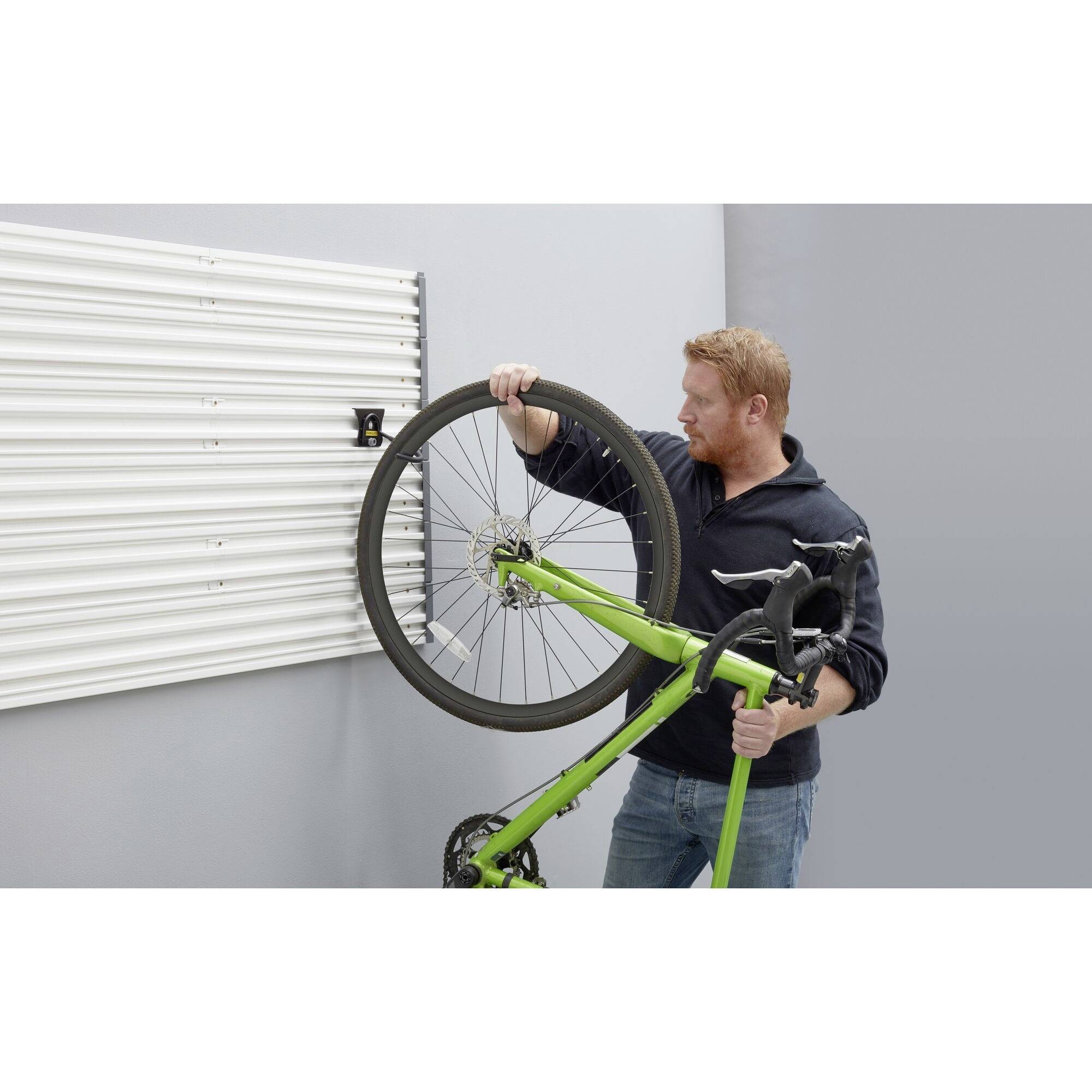 Ein Mann hängt ein Fahrrad an die Wand. Das Fahrrad ist grün mit einem schwarzen Reifen. Die Wand ist mit einer Rille ausgestattet.