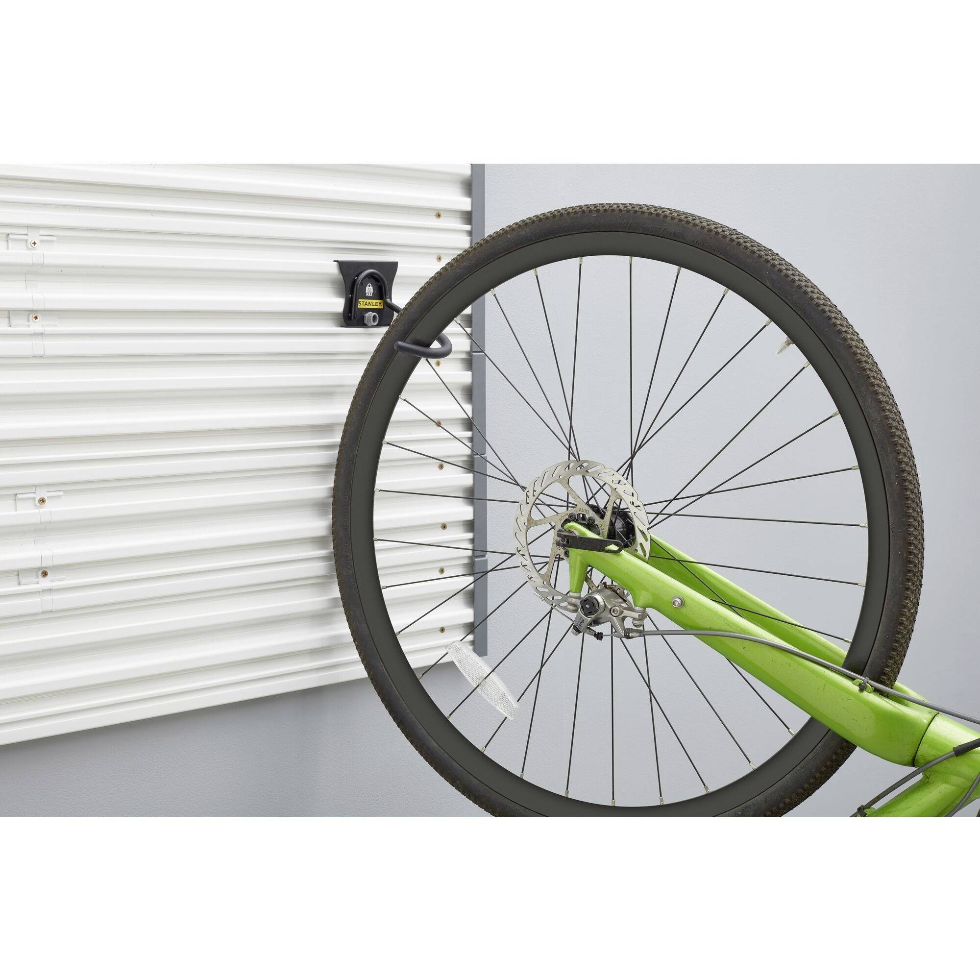 Ein grünes Fahrrad ist an einer weißen, geriffelten Wand aufgehängt. Das Vorderrad ist sichtbar, befestigt mit einem schwarzen Halter.