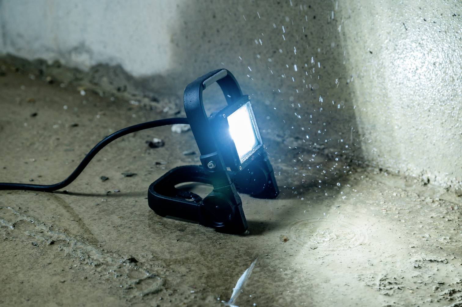 Scheuern des Wassersprays auf einem leuchtenden Arbeitsstrahler, der auf einem Betonboden in einer Ecke platziert ist.