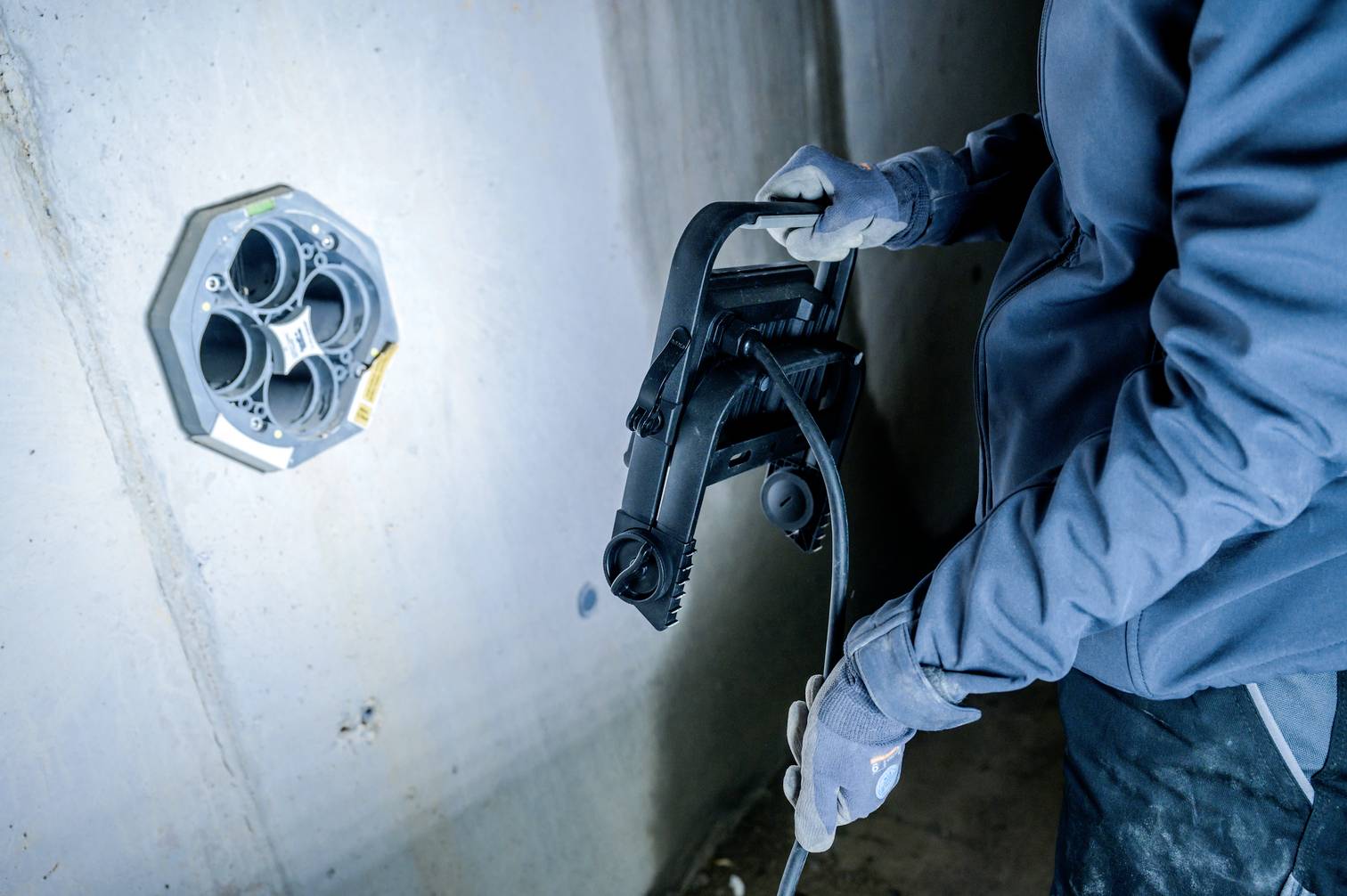 Eine Person arbeitet an einer Wandinstallation mit einem Kabel. Die Szene zeigt technische Arbeitsschritte und die Handhabung von Werkzeugen.