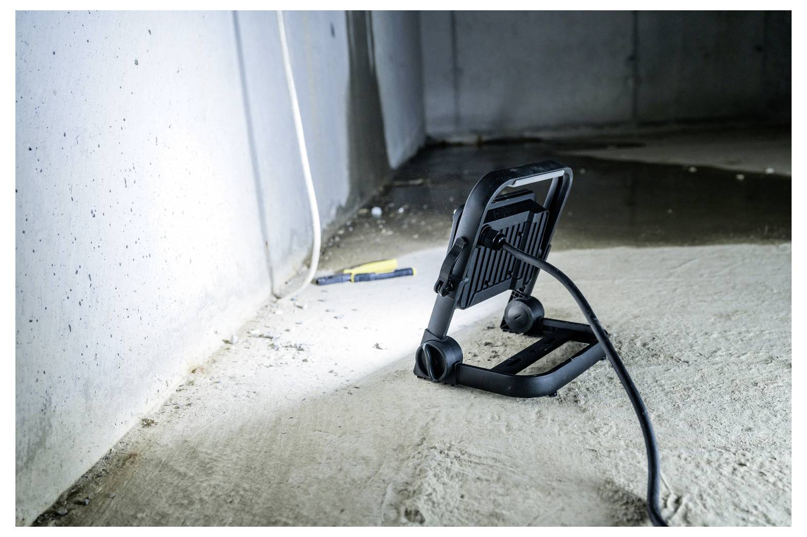 Tragbare Arbeitsleuchte, die auf einem Betonboden in einem unfertigen Raum steht, mit ihrem Stromkabel, das über den Boden verläuft, und einem Schraubendreher in der Nähe.
