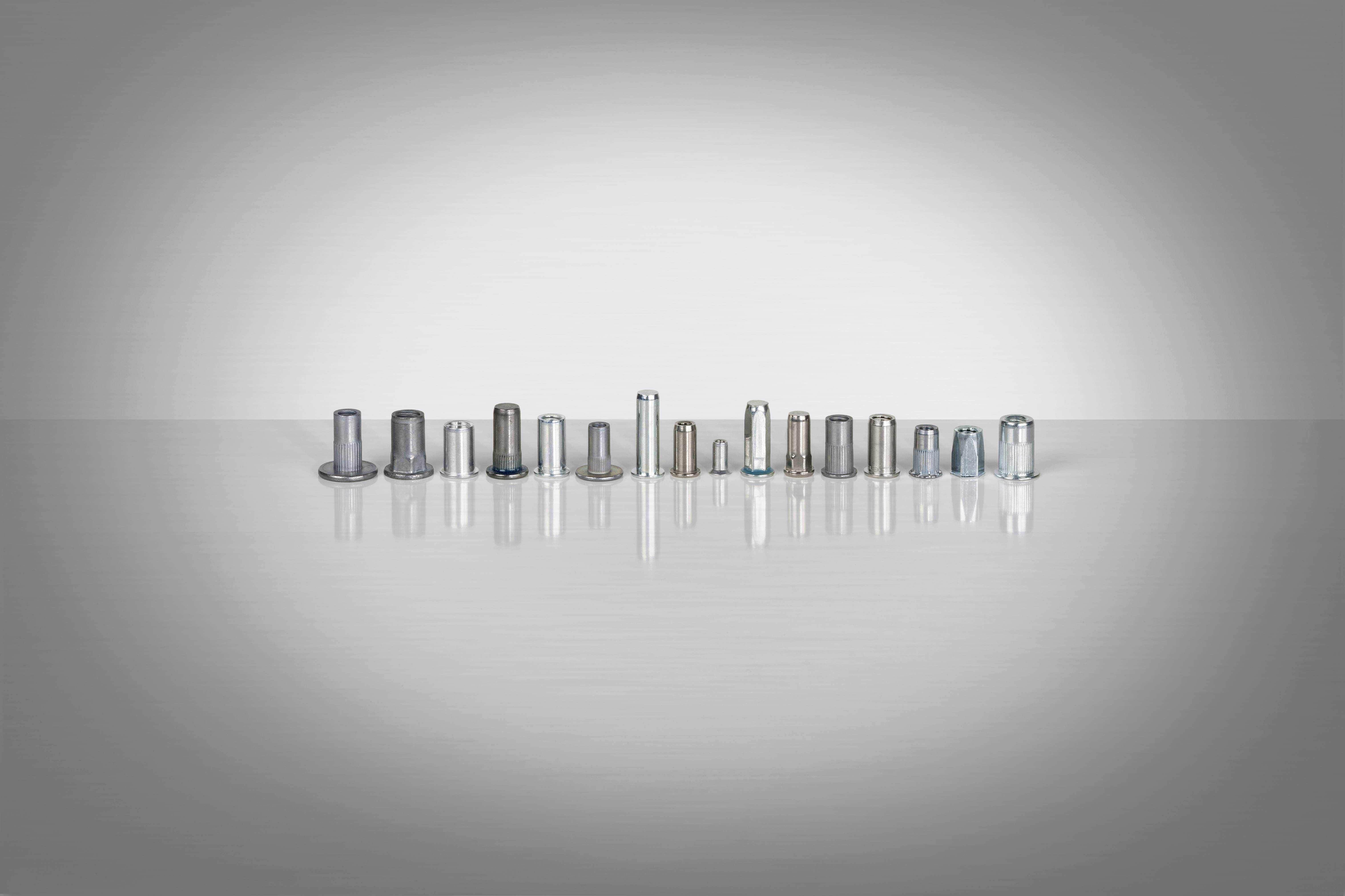 Verschiedene Gewindehülsen aus Metall in einer Reihe auf einer reflektierenden Oberfläche dargestellt, ohne weiteren Kontext.