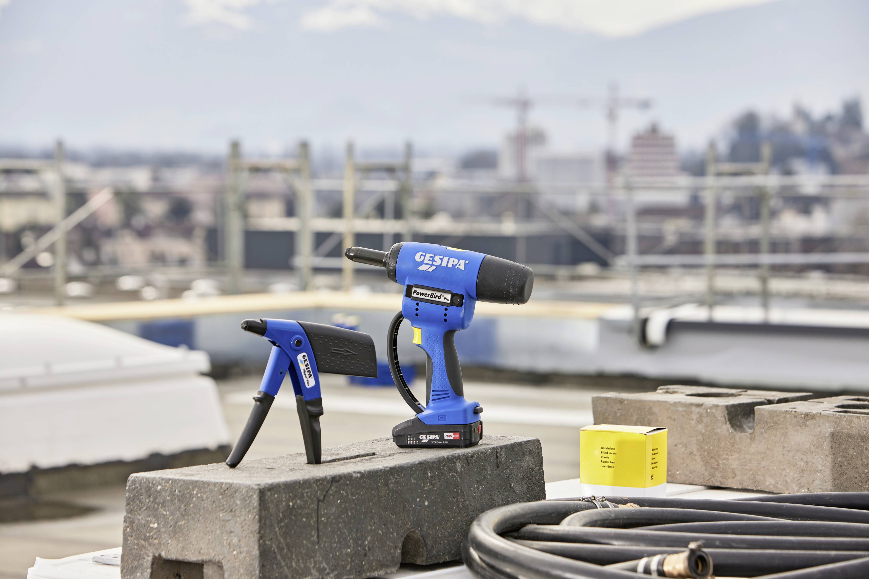 Auf einem Dach sitzende Nietwerkzeuge mit einem blauen, modernen Design, im Hintergrund eine unscharfe Stadtlandschaft.