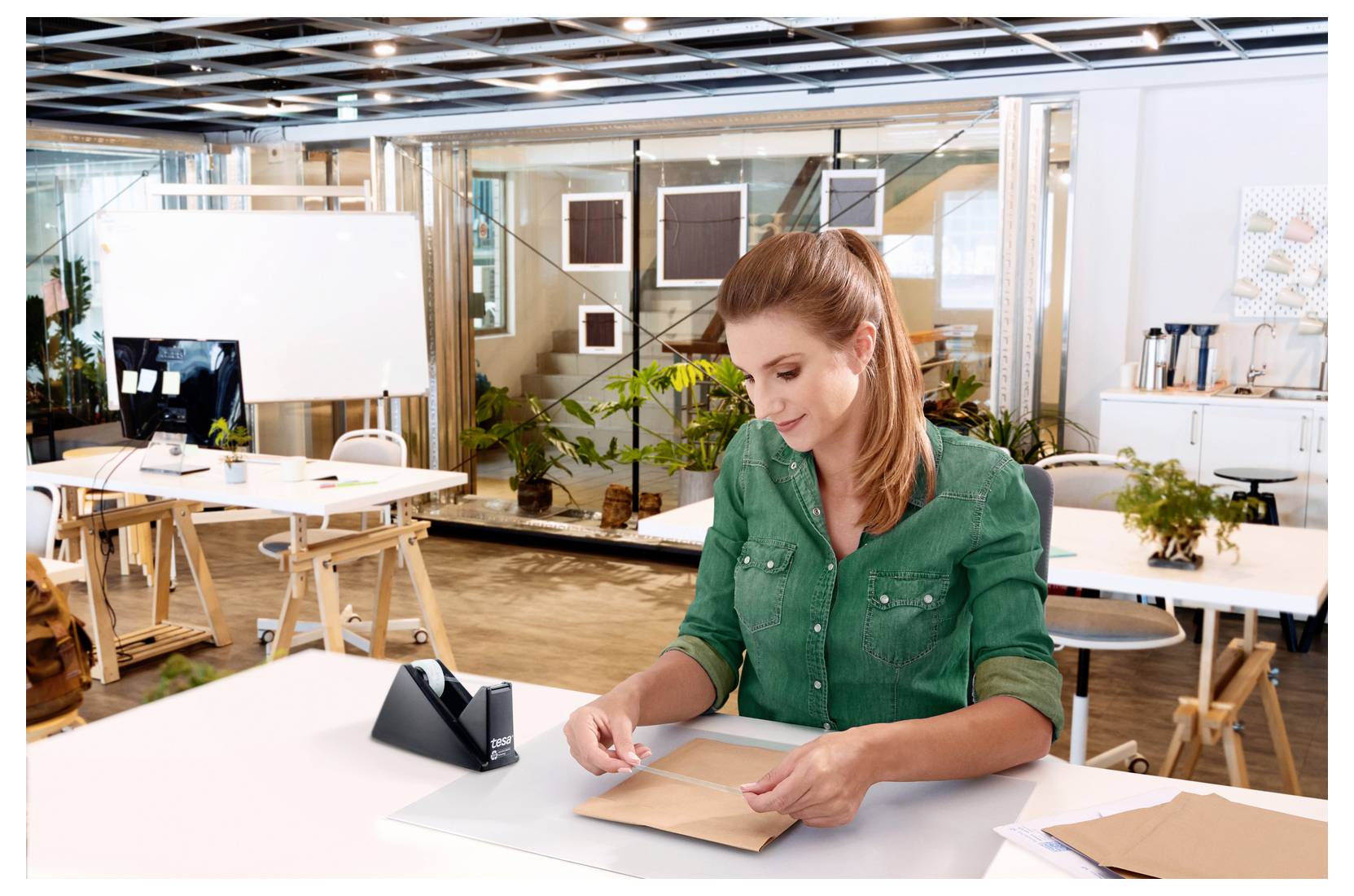 Eine Frau in einem modernen Büro klebt einen Umschlag zu. Der Raum ist hell und mit Pflanzen dekoriert, was eine angenehme Arbeitsatmosphäre schafft.