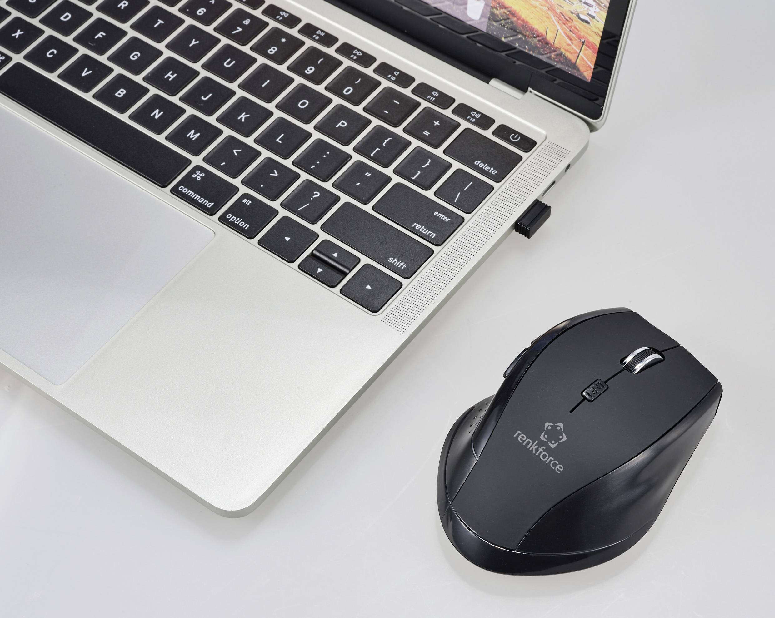 Ein Laptop mit geöffnetem Deckel und einer kabellosen Maus daneben auf einem weißen Tisch.