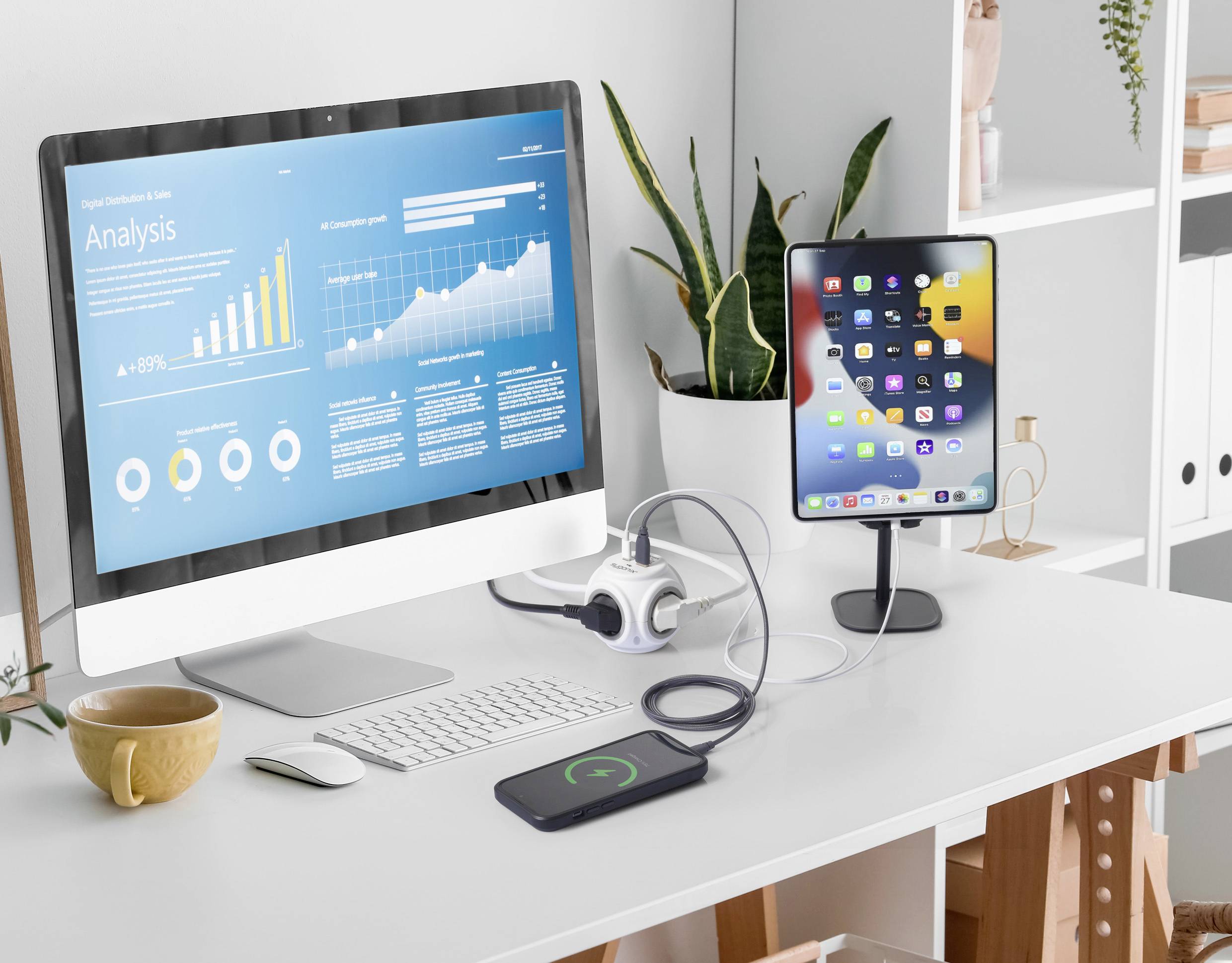 Ein moderner Schreibtisch mit Computermonitor zeigt Datenanalysen. Ein Tablet, Smartphone und Pflanzen sind ebenfalls auf dem Tisch.