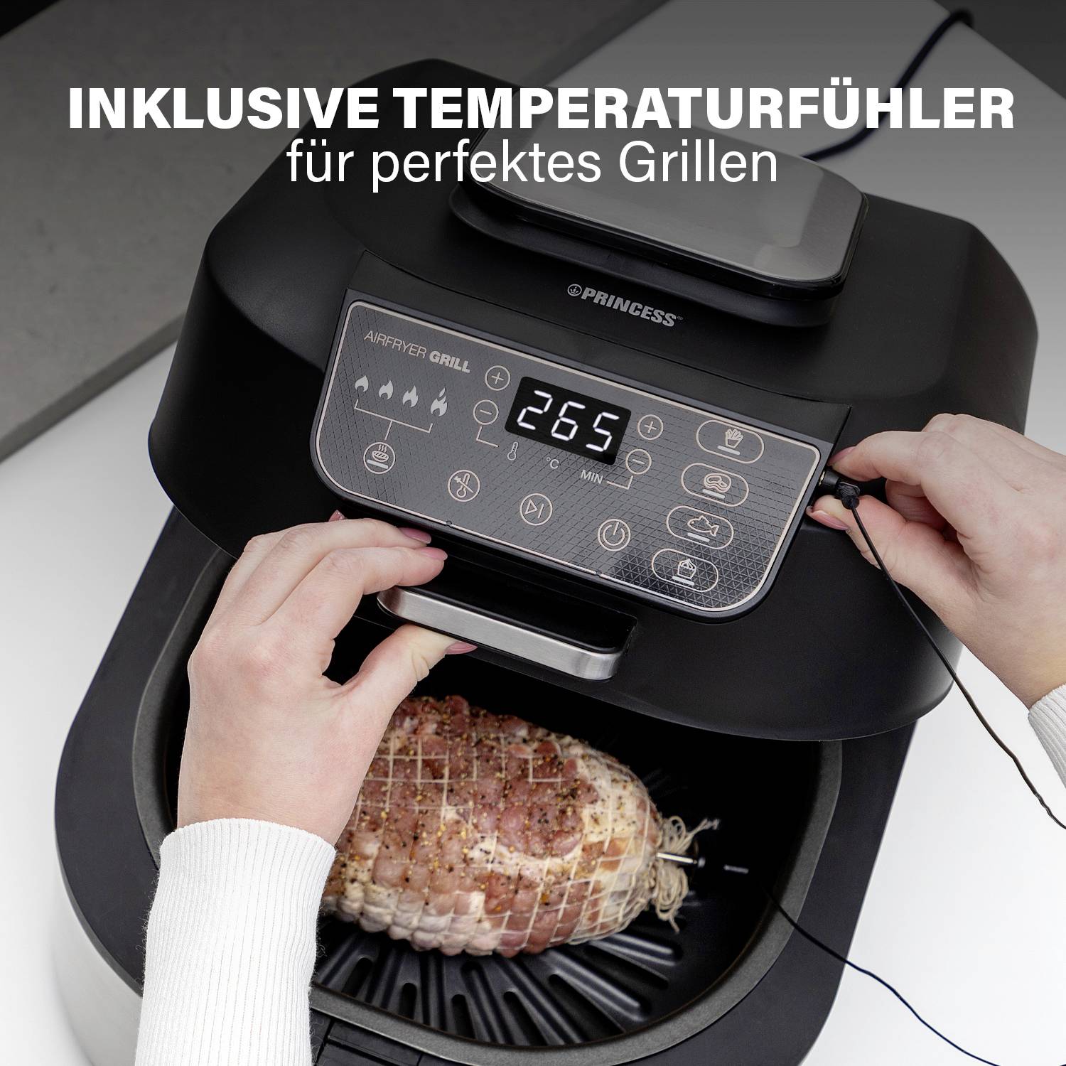 Luftfritteuse mit digitalem Display zeigt 267°C. Zwei Hände richten einen Temperaturfühler in ein Fleischstück ein. Text: 'Inklusive Temperaturfühler für perfektes Grillen'.