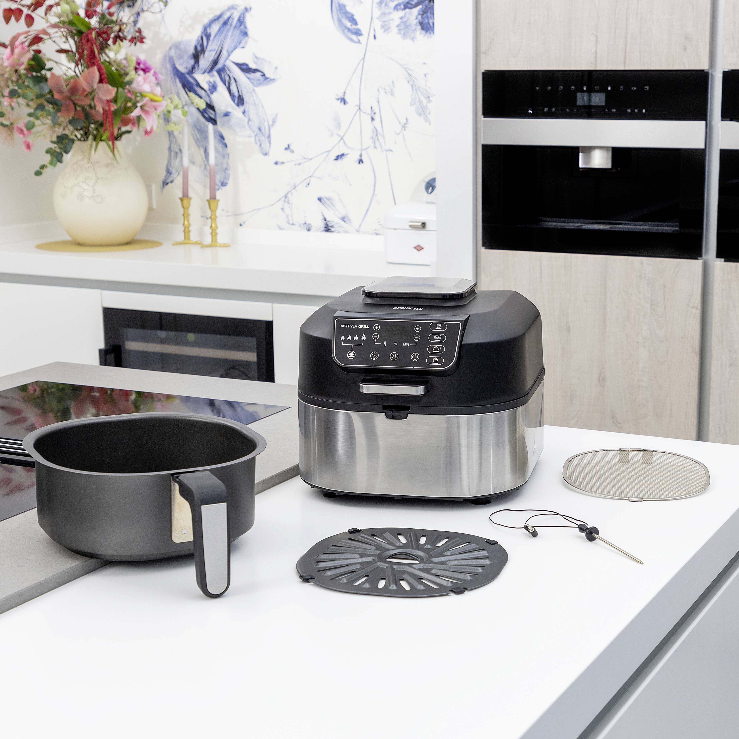 Eine moderne Küche mit einem Luftfritteusen-Gerät auf der Arbeitsplatte, neben einem Kochtopf und Küchenutensilien. Im Hintergrund ist ein Backofen sichtbar.