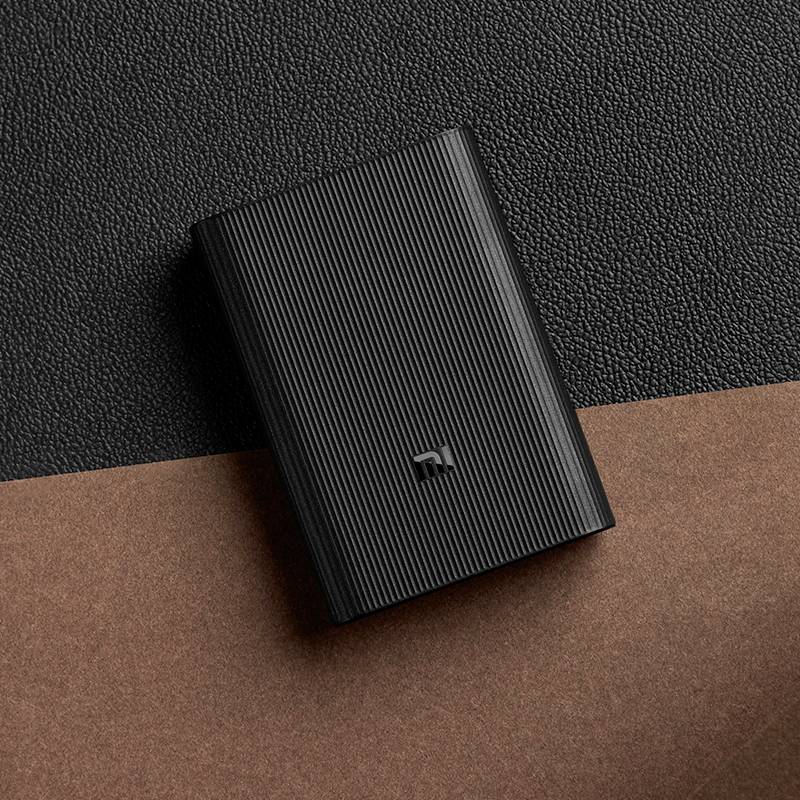 Eine schwarze, strukturierte Powerbank liegt auf einer zweifarbigen Oberfläche aus schwarzem und braunem Material.