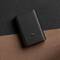 Eine schwarze, strukturierte Powerbank liegt auf einer zweifarbigen Oberfläche aus schwarzem und braunem Material.