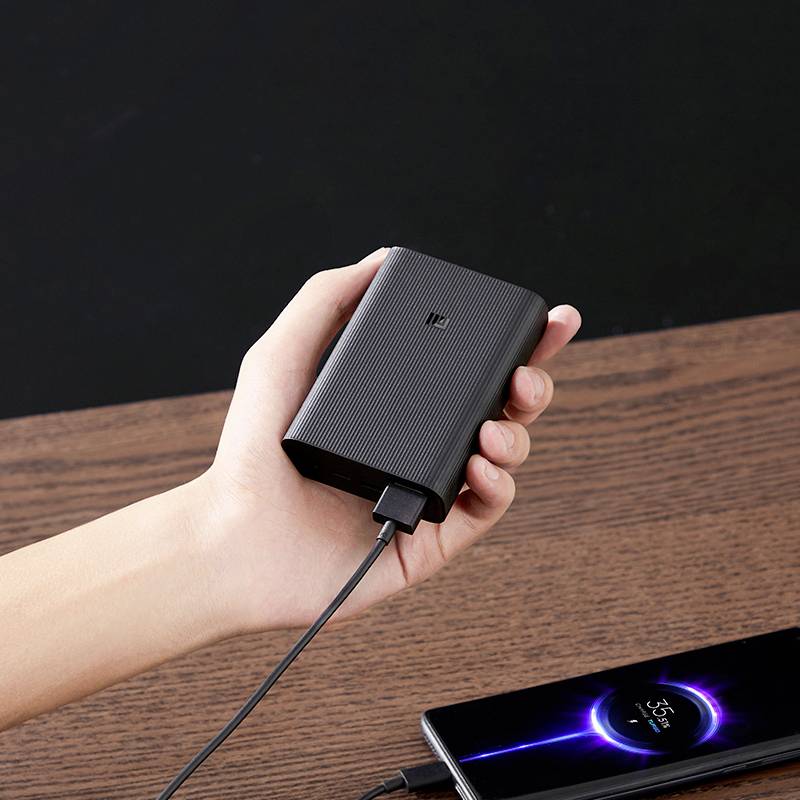 Eine Hand hält eine Powerbank, die ein Smartphone auflädt. Das Smartphone zeigt einen Ladevorgang mit einem Energieanzeigesymbol.