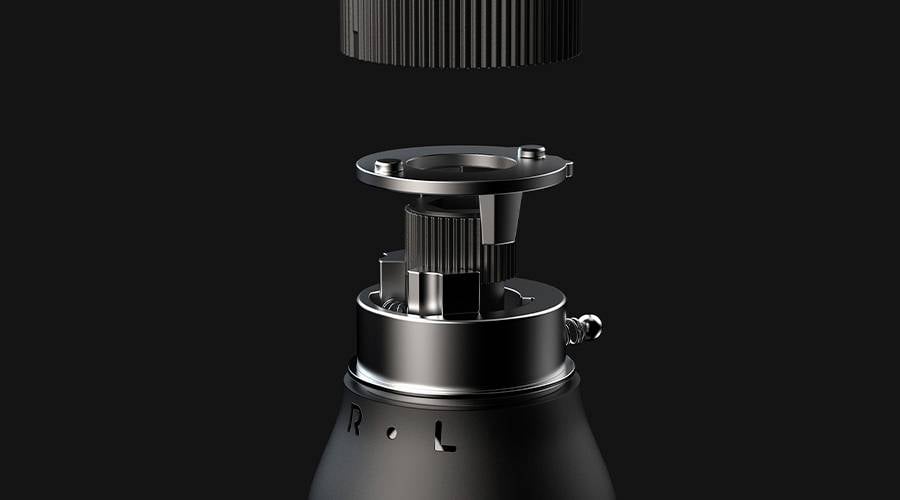 Nahaufnahme eines technischen Geräts in Einzelteilen auf schwarzem Hintergrund. Zeigt obere mechanische Bauteile einer Maschine.