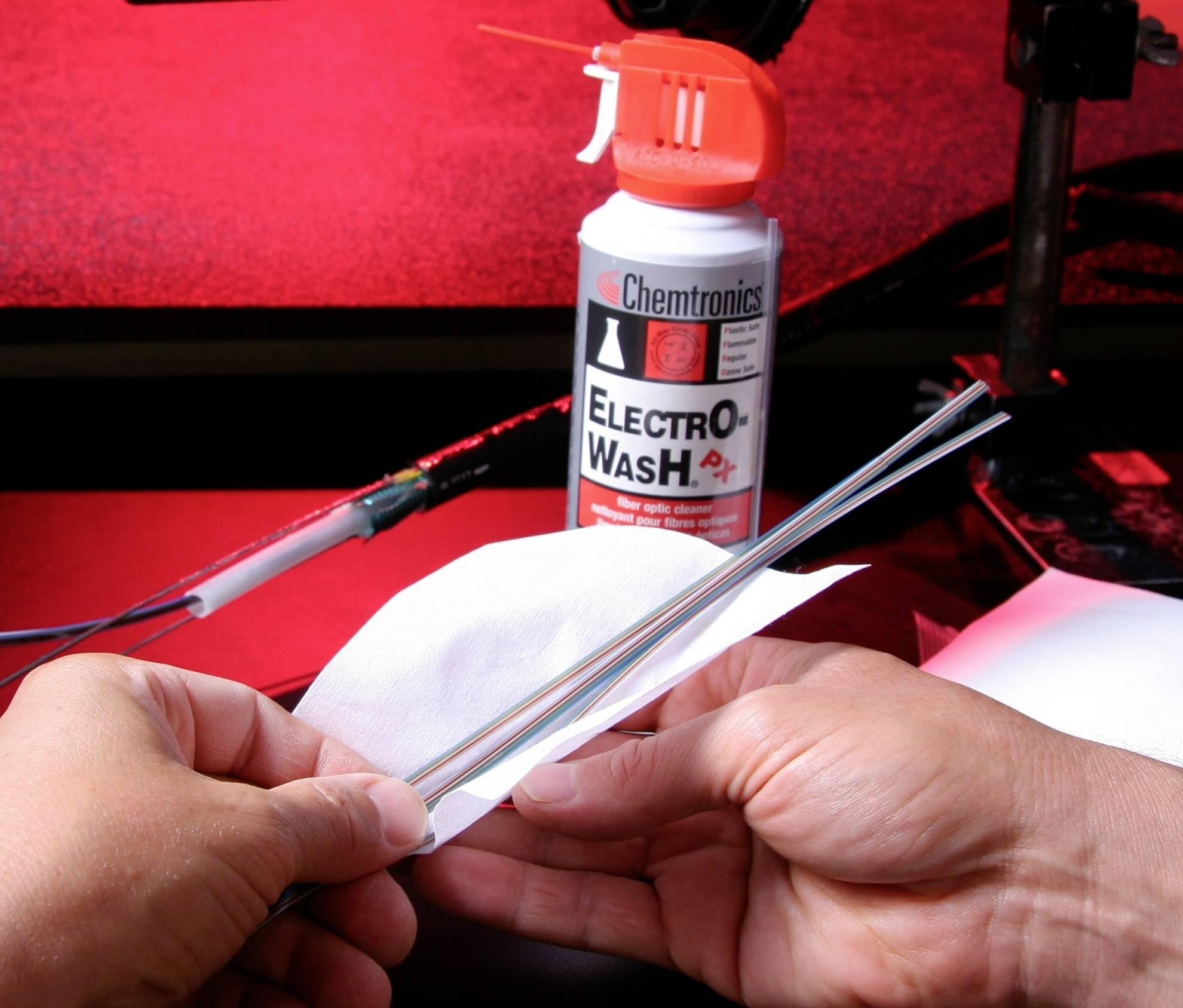Eine Person reinigt eine Metallstange mit einem weißen Tuch. Im Hintergrund steht eine Dose 'Electro-Wash' auf einem roten Tisch.