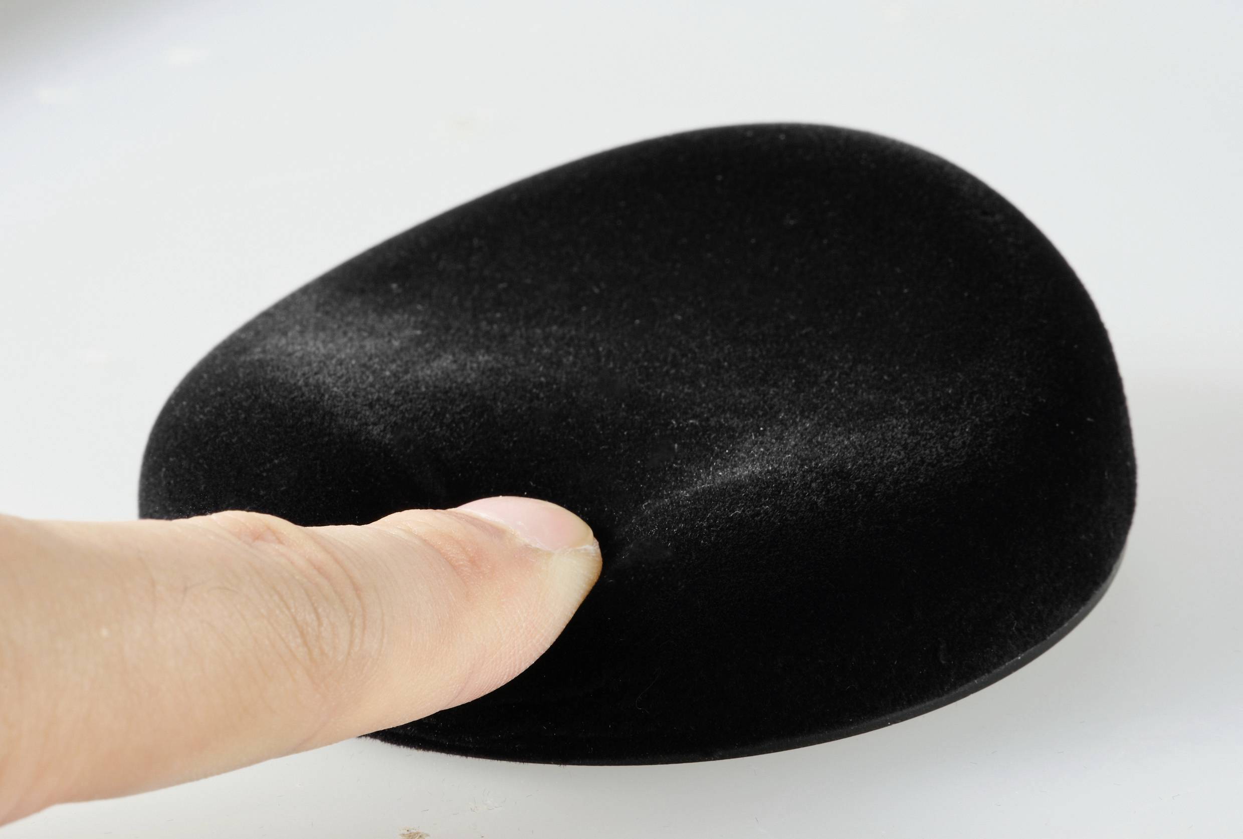 Eine Hand drückt leicht auf ein schwarzes, ovales Anti-Stress-Spielzeug, das auf einer weißen Oberfläche liegt.