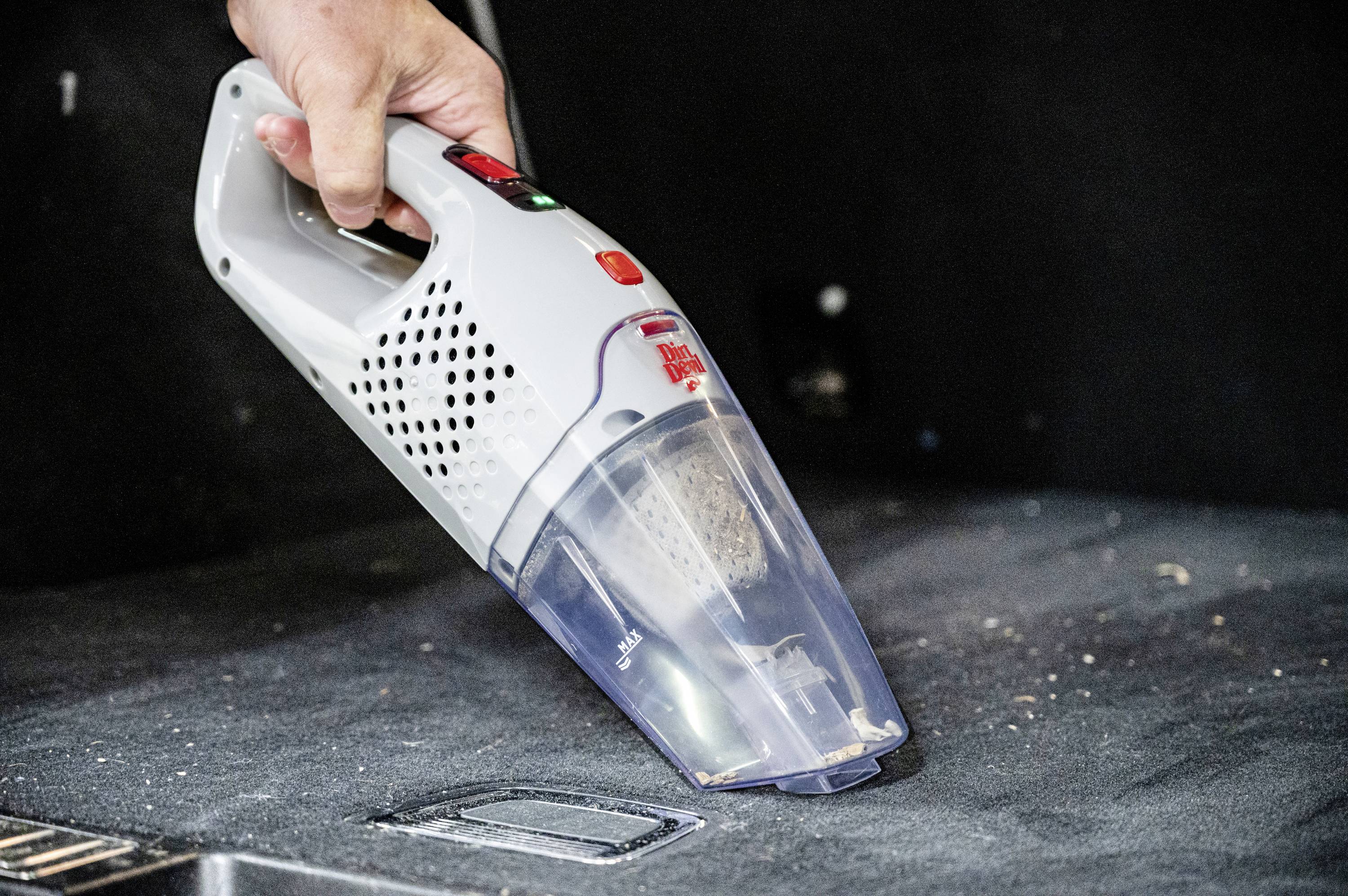 Hand hält einen tragbaren Staubsauger und reinigt eine dunkle Oberfläche von Krümeln und Staub.