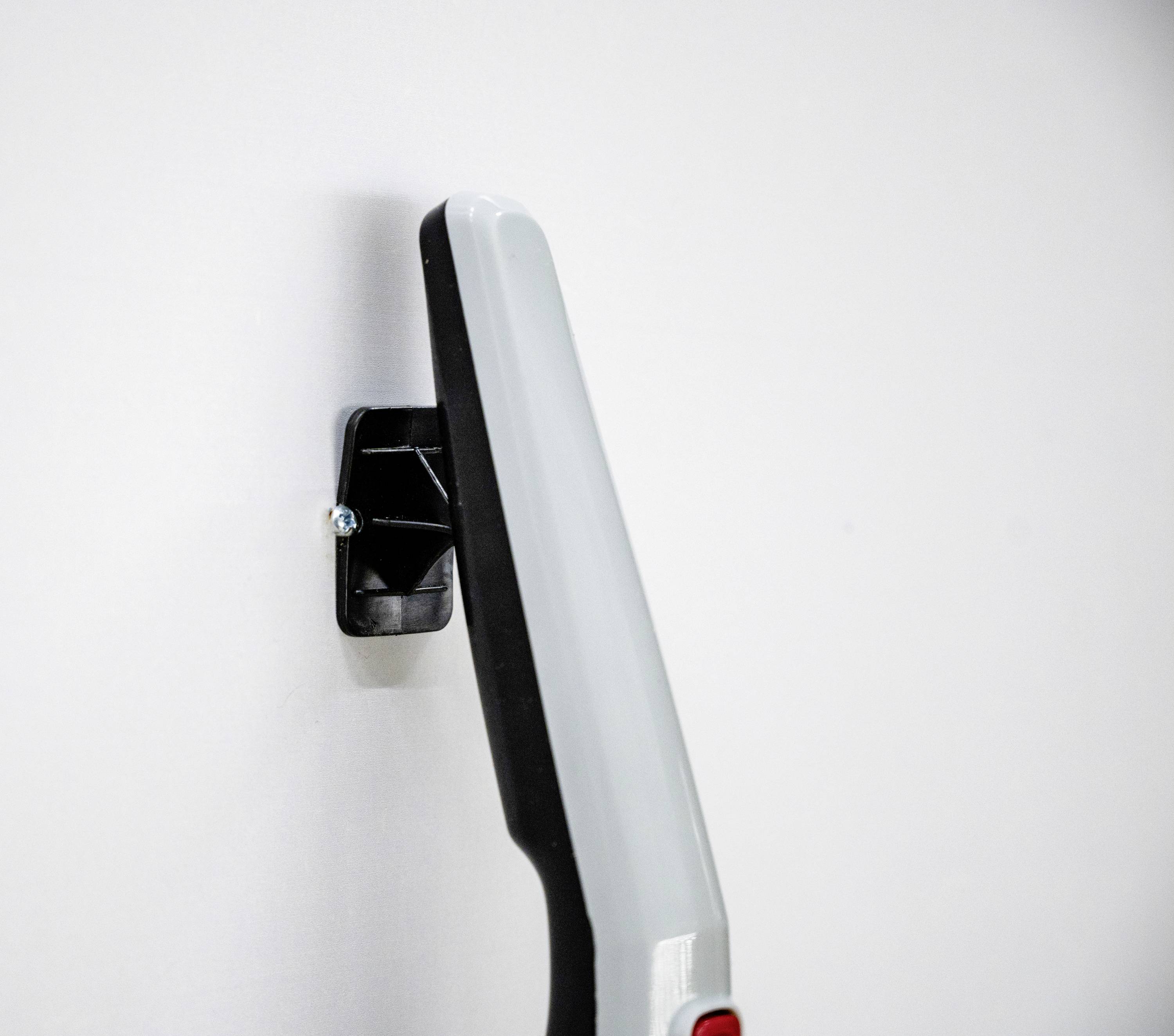 Ein grauer Griff ist an einer weißen Wand befestigt. Der Griff hat einen schwarzen Sockel und scheint ergonomisch geformt zu sein.
