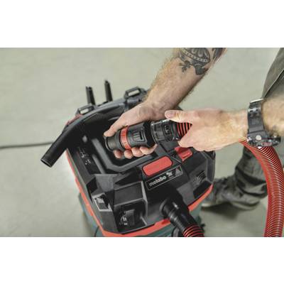 Eine Person verbindet einen roten Schlauch mit einem Metabo Industriesauger. Fokus liegt auf den Händen und dem Anschluss des Schlauches.
