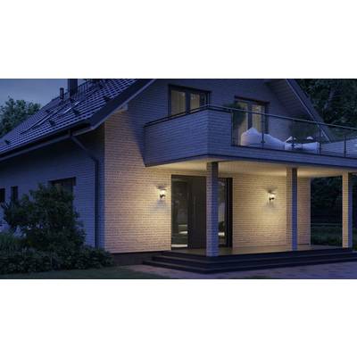 Ein modernes zweistöckiges Haus bei Nacht, beleuchtet durch Außenlampen auf der Terrasse. Balkontüren und Fenster zeigen Innenlicht.