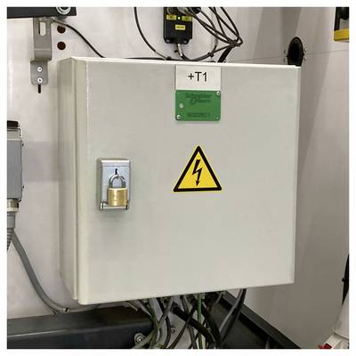 Verschlossener elektrischer Schaltschrank mit der Bezeichnung „+T1", Hochspannungswarnzeichen und angeschlossene Kabel in einer Industrieumgebung.