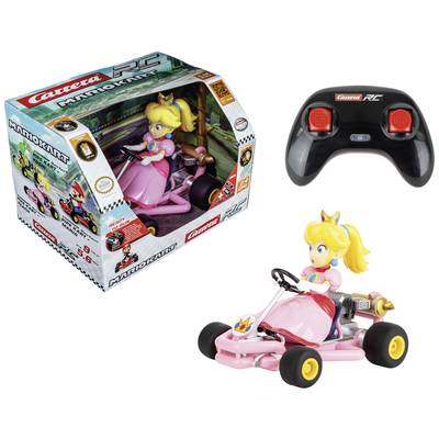 Eine Spielzeugfigur in einem rosa Kart fährt fernsteuerbar. Verpackung zeigt dieselbe Figur und Fernbedienung. Thema: 'Mario Kart'.