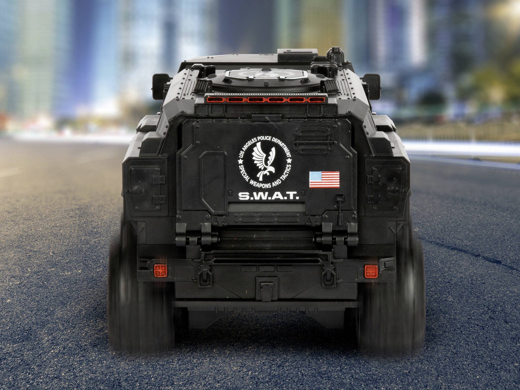 Schwarzes gepanzertes SWAT-Fahrzeug auf leerer Straße vor unscharfem städtischem Hintergrund. USA-Flagge und SWAT-Emblem hinten.