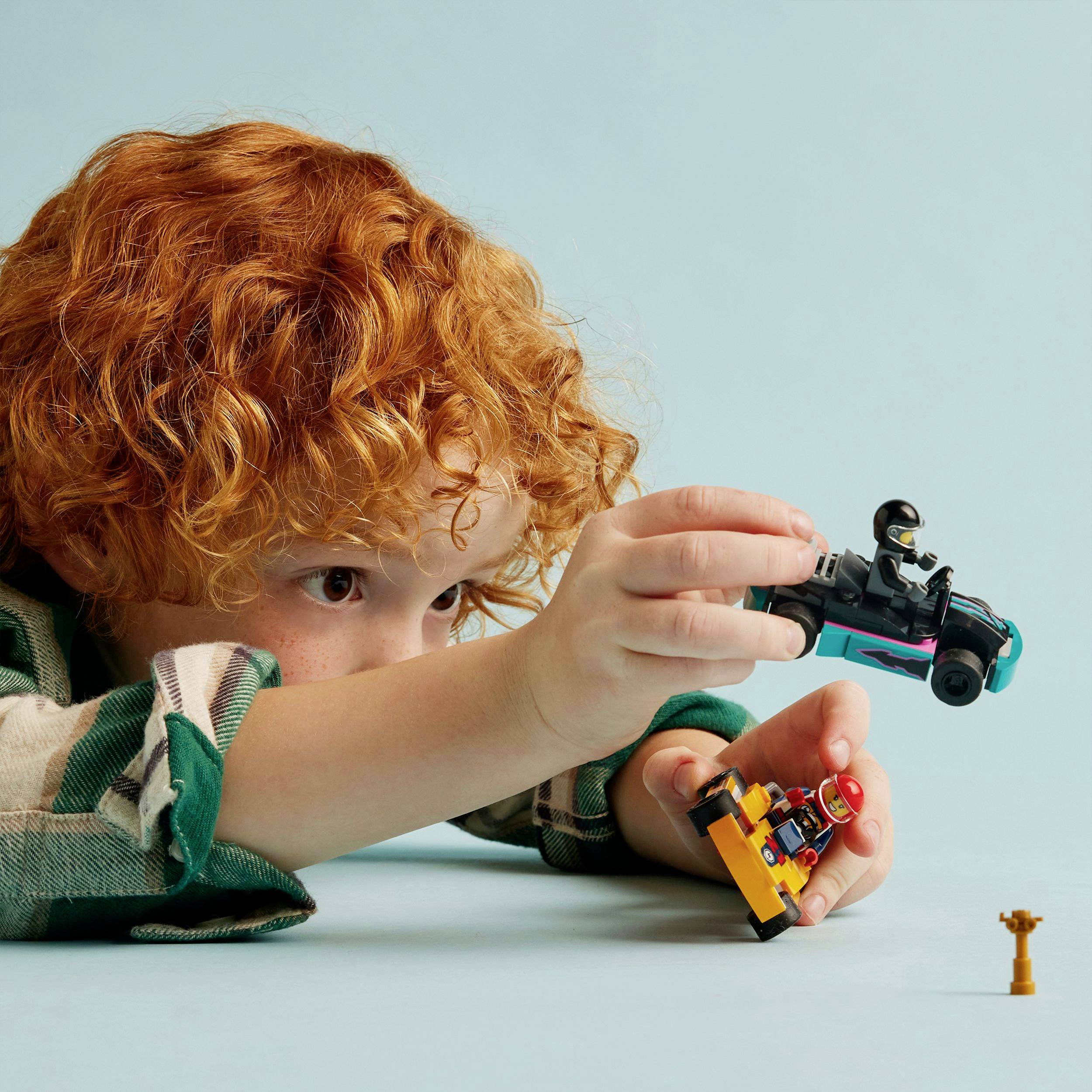 Ein Kind spielt konzentriert mit zwei Spielzeugautos auf einem Tisch. Im Hintergrund steht eine kleine, gelbe Trophäe.