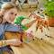 Ein Kind spielt mit Lego-Tierfiguren, darunter eine Giraffe und ein Baum. Im Hintergrund sind weitere Spielsachen und eine Pflanze zu sehen.