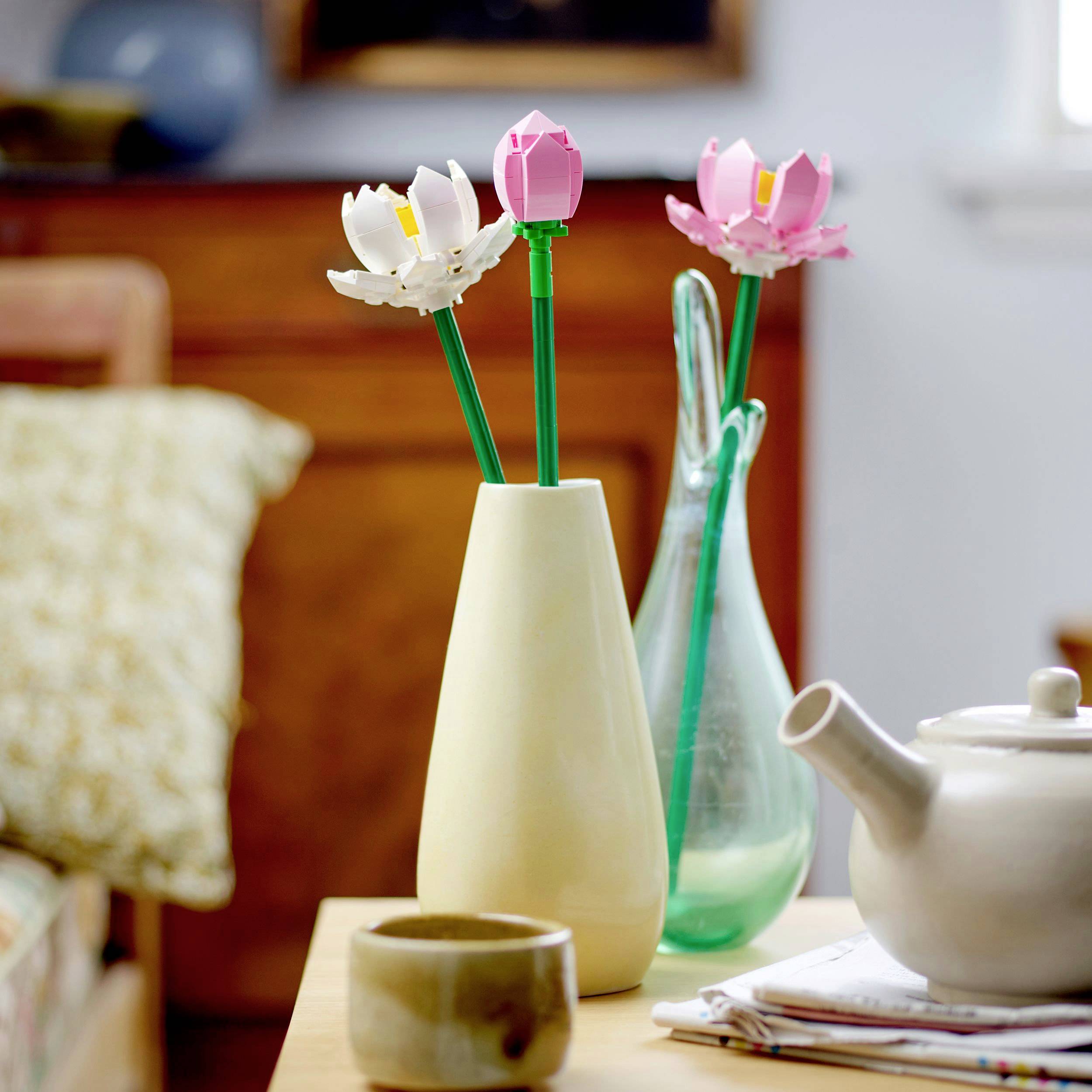 Eine Vase mit kunstvollen Blumen aus Metall oder Kunststoff auf einem Tisch neben einem Teekrug und einer hölzernen Schale.