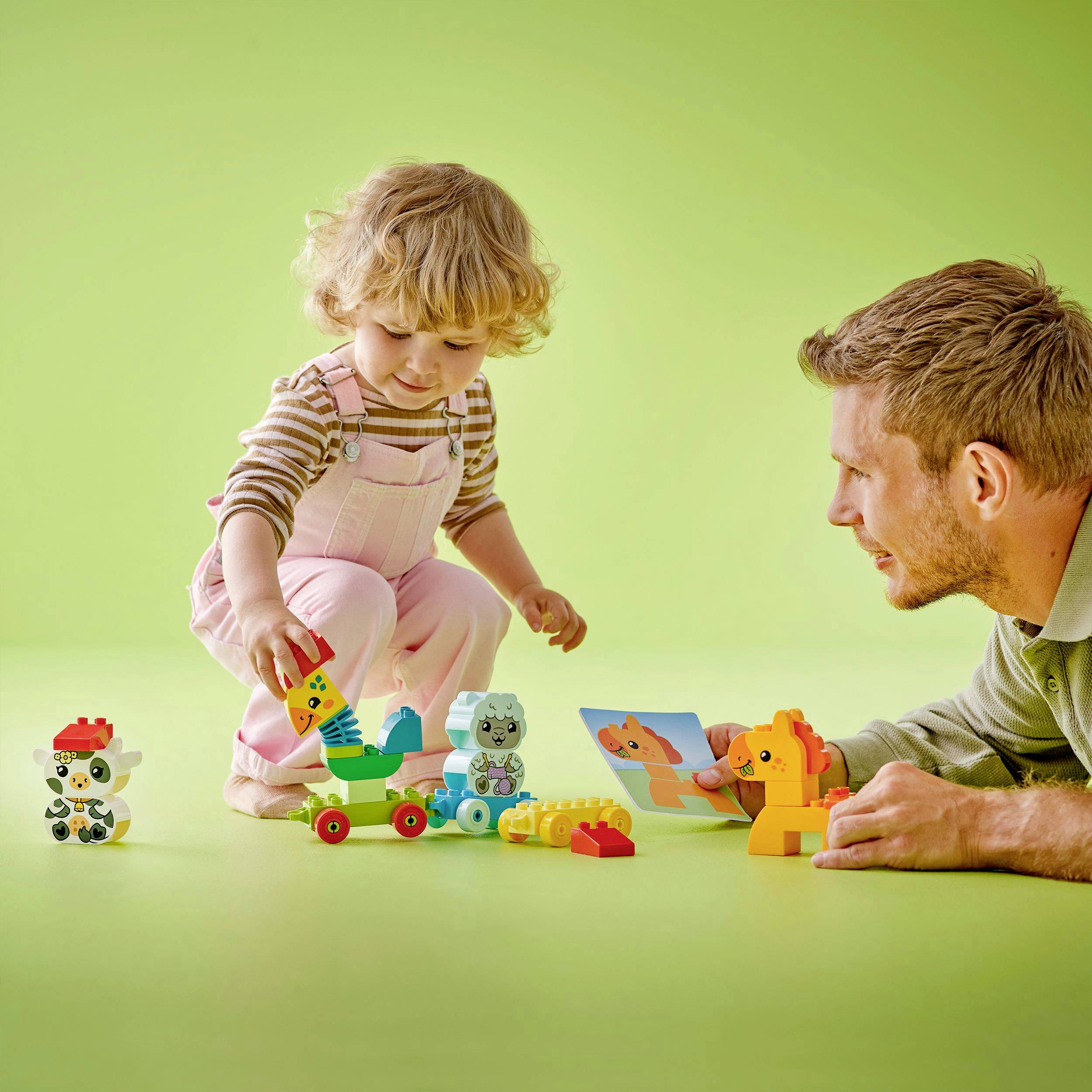 Ein Kleinkind und ein Erwachsener spielen gemeinsam mit buntem LEGO Duplo auf einem Tisch. Spielzeugfiguren und Bauklötze sind verstreut.