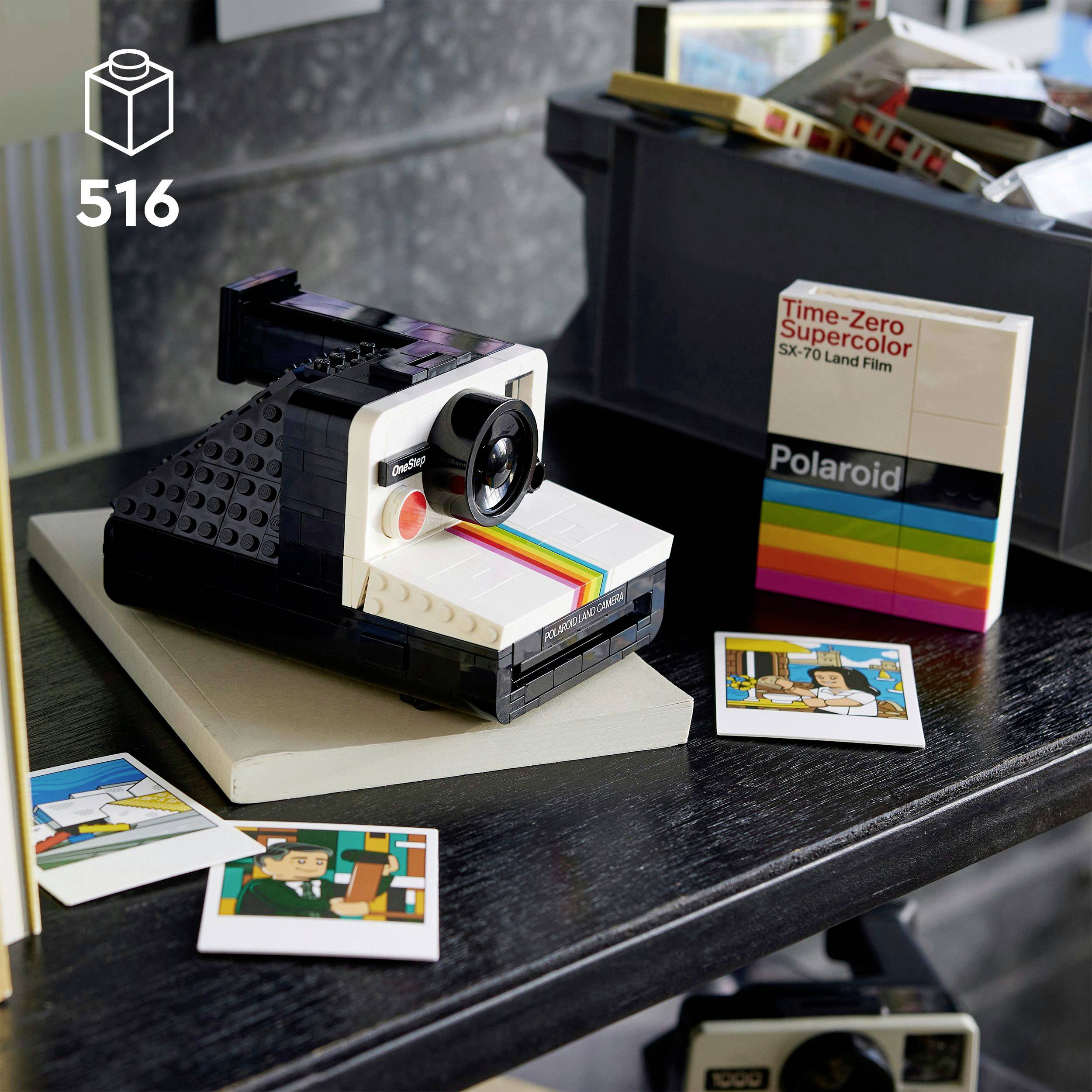 Auf einem Tisch steht eine aus Lego gebaute Polaroid-Kamera, umgeben von Polaroid-Fotos und einer Filmverpackung.