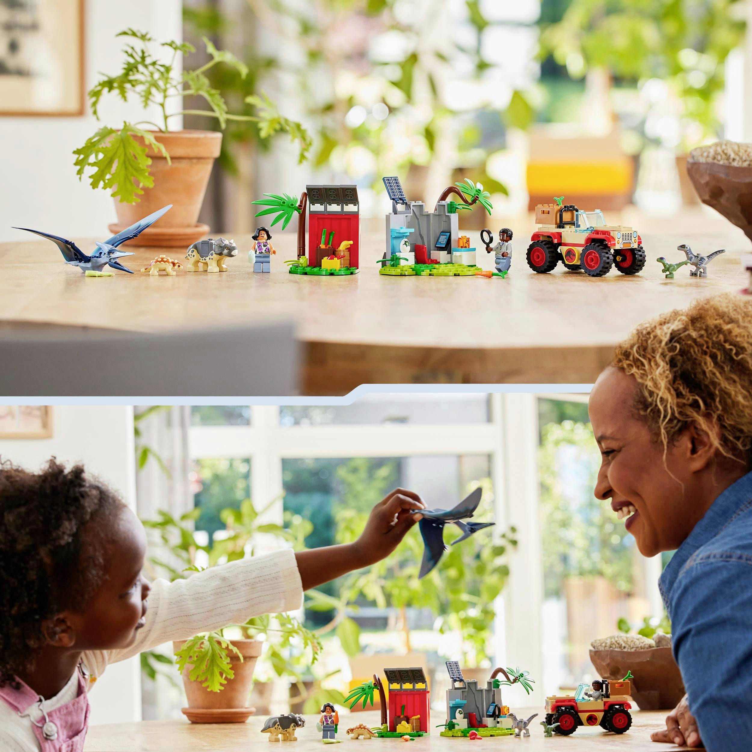 Ein Kind und eine erwachsene Person spielen mit einem Dinosaurier-Spielzeugset auf einem Tisch. Im Hintergrund sind Pflanzen zu sehen.