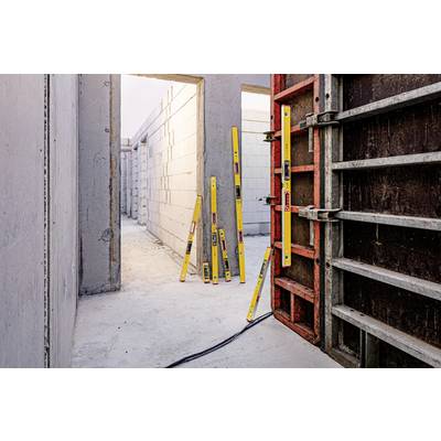Mehrere gelbe Wasserwaagen lehnen im Rohbau eines Gebäudes an einer Betonwand, umgeben von unvollendeten Betonwänden und Türen.