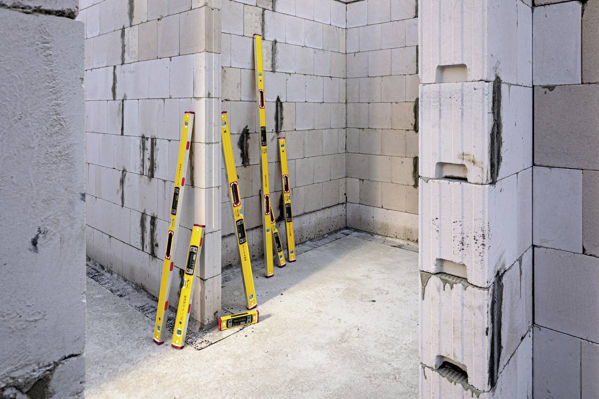 Eine Baustelle mit vier gelben Wasserwaagen, die an Wänden aus Mauersteinen lehnen, zeigt eine begonnene Baukonstruktion.