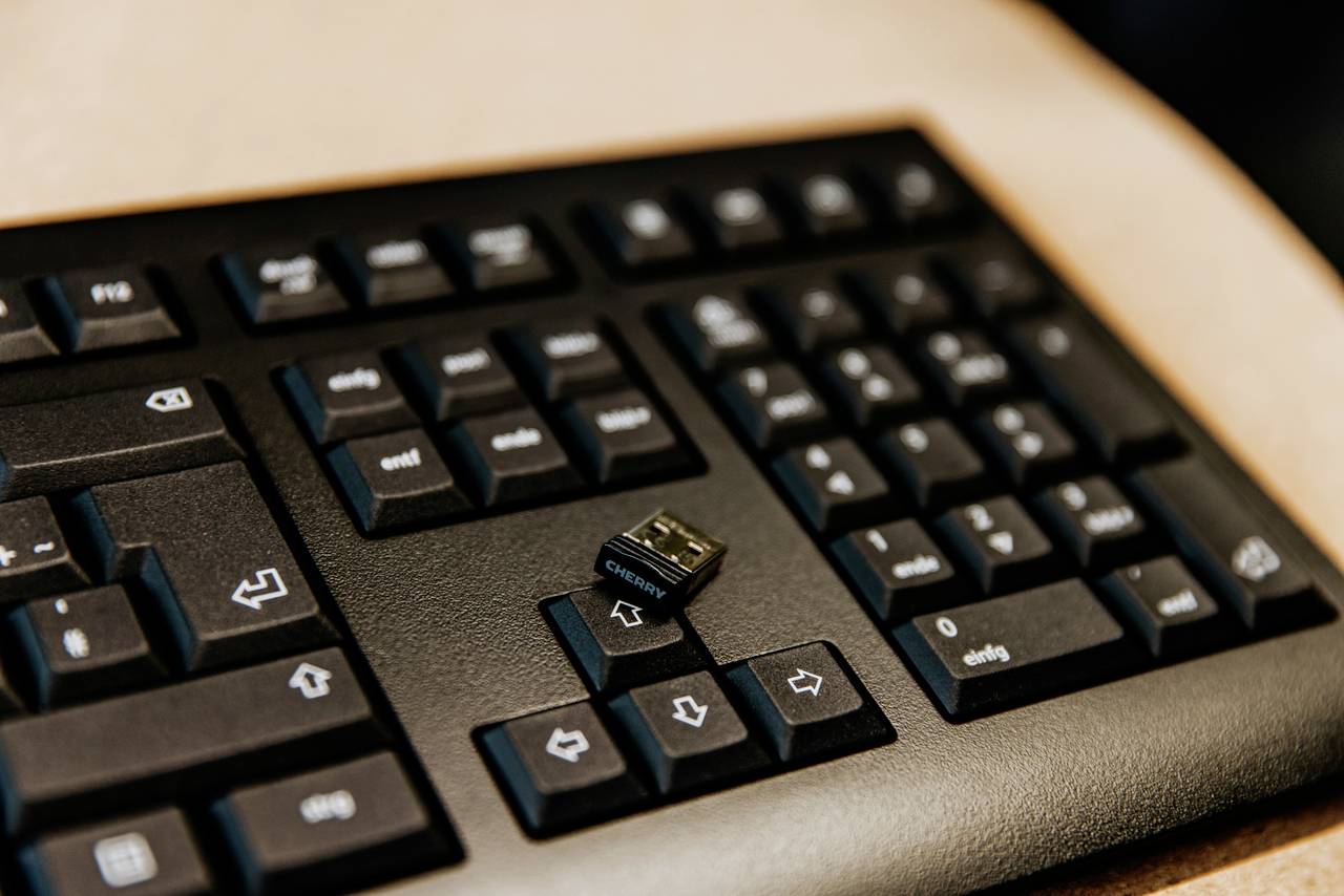 Eine schwarze Computertastatur mit einem kleinen USB-Dongle, der auf den Tasten liegt.